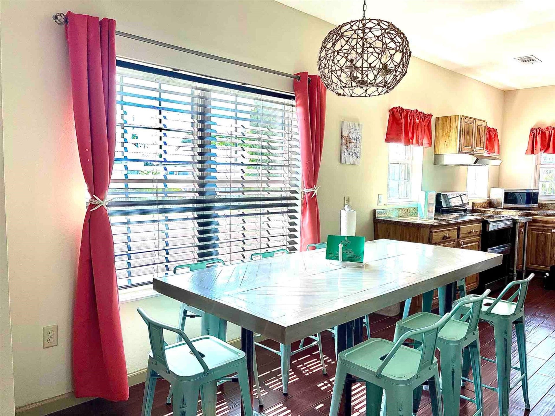 Bright and inviting kitchen with a large window, modern chandelier, and a spacious dining area featuring a sleek table and colorful chairs.