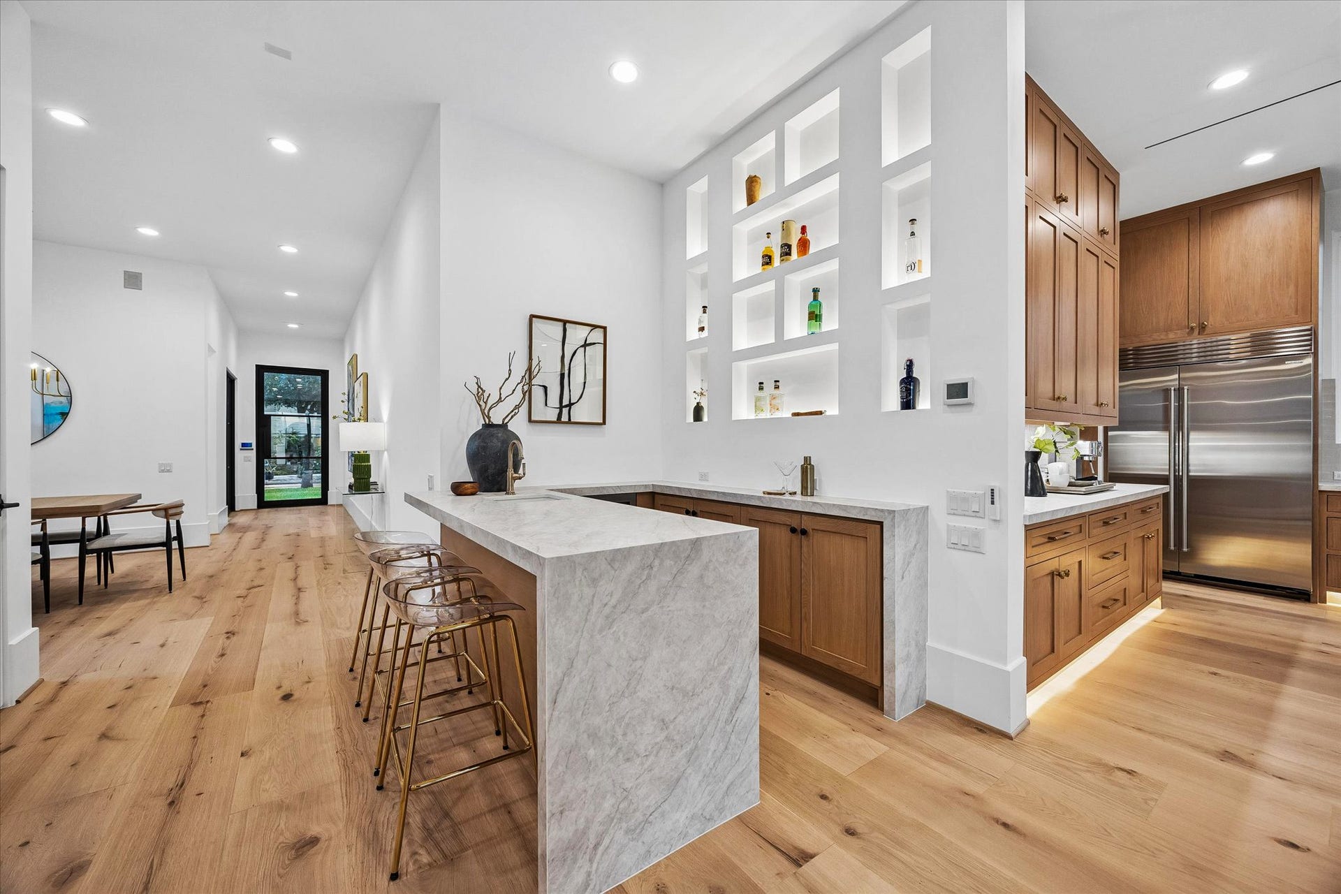 [Home Bar] Why go out when you can bring the party to your place? Perfect setting for gatherings large and small. Quartz waterfall counter with space for bar seating; bar sink; illuminated display shelving; under-counter Zephyr beverage refrigerator.