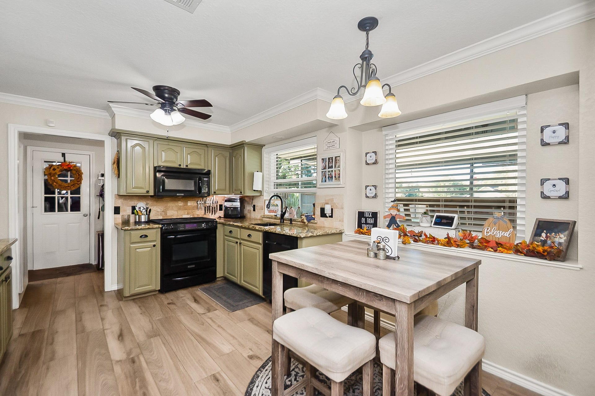 928 Oleander Street, Lake Jackson, TX 77566 Charming kitchen with olive green cabinets, modern black appliances, and a cozy breakfast nook by a large window, offering ample natural light and a welcoming atmosphere.