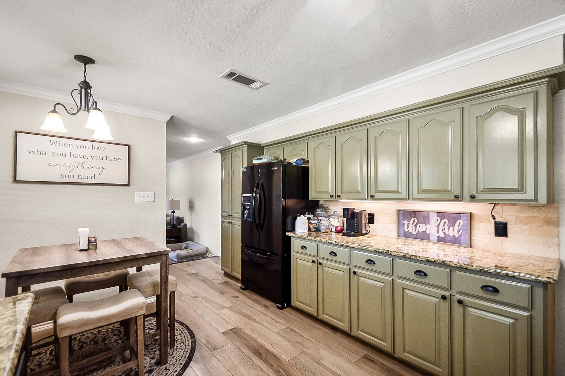 928 Oleander Street, Lake Jackson, TX 77566 Charming kitchen with sage green cabinetry, granite countertops, and a cozy dining area under warm pendant lighting, perfect for intimate meals.