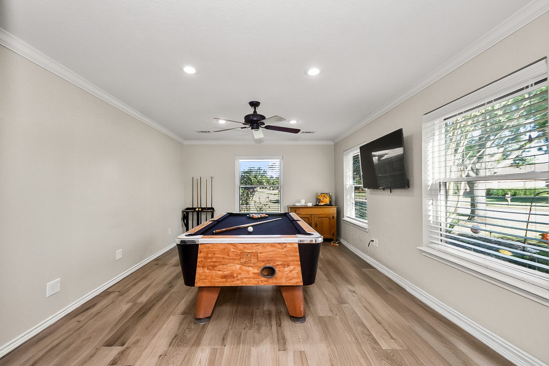 928 Oleander Street, Lake Jackson, TX 77566 Spacious game room featuring a stylish pool table, sleek wood look flooring, and abundant natural light from large windows, perfect for entertaining and relaxation.