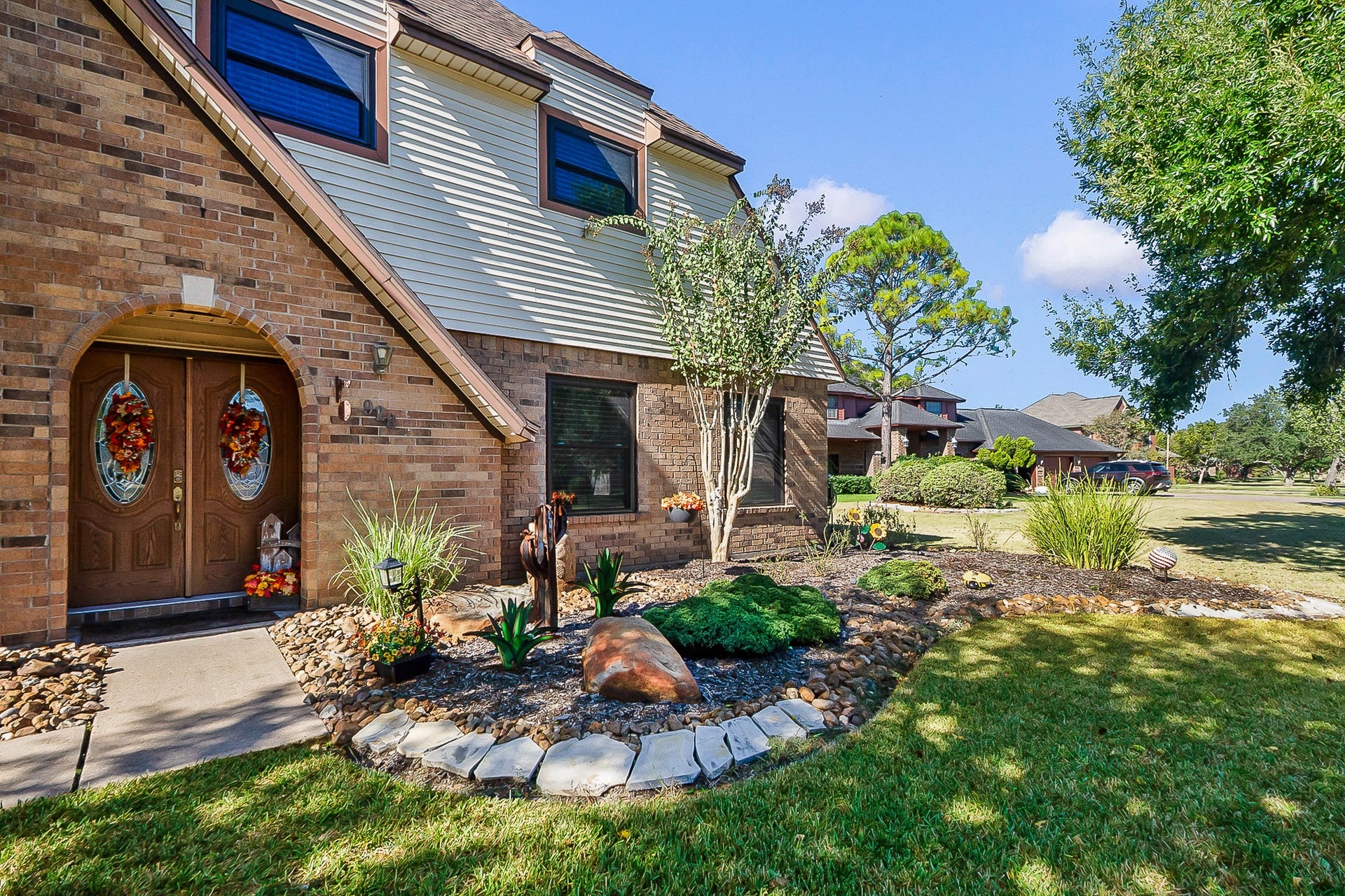 928 Oleander Street, Lake Jackson, TX 77566 Charming two-story home with a classic brick exterior, welcoming double doors adorned with seasonal decor, and beautifully landscaped front yard featuring lush greenery and stone accents.