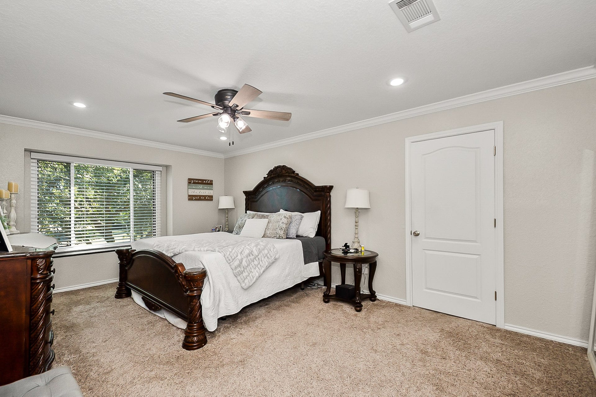 928 Oleander Street, Lake Jackson, TX 77566 Spacious Primary bedroom featuring plush carpeting, a ceiling fan, and a large window inviting natural light, complemented by elegant wooden furniture for a cozy retreat.