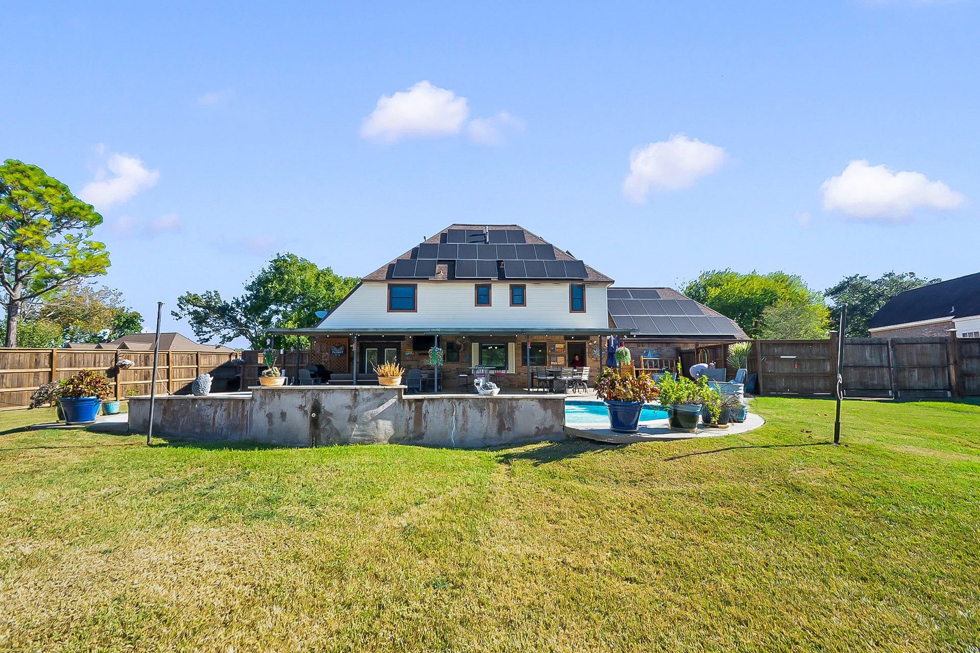 928 Oleander Street, Lake Jackson, TX 77566 Expansive backyard with lush green lawn, featuring a charming two-story home equipped with paid off solar panels. Enjoy outdoor living with a spacious patio and a well-maintained pool surrounded by potted plants, perfect for relaxation and entertaining.