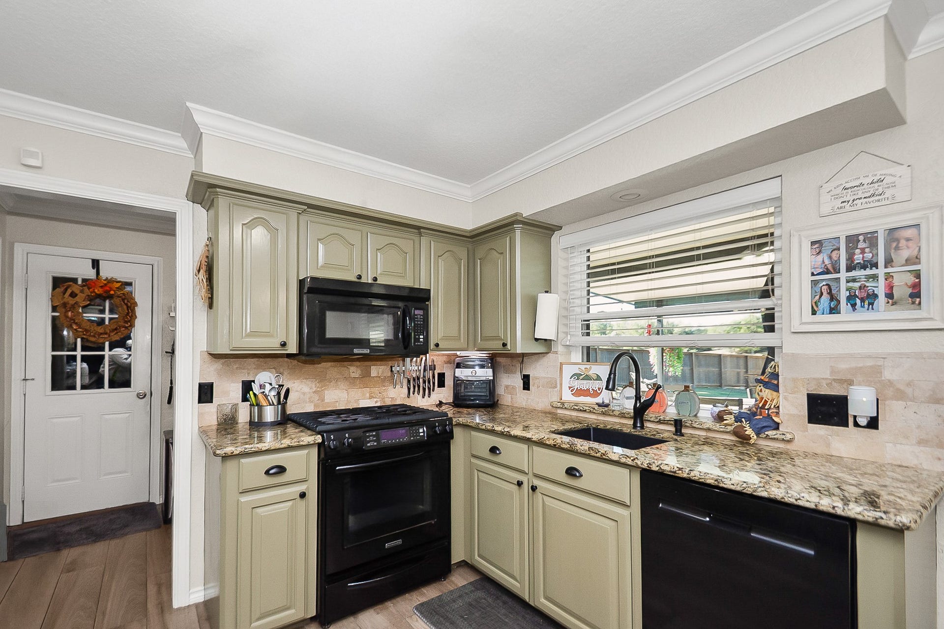 928 Oleander Street, Lake Jackson, TX 77566 Charming kitchen with sage green cabinets, granite countertops, and a cozy window view, featuring modern appliances and a convenient layout.