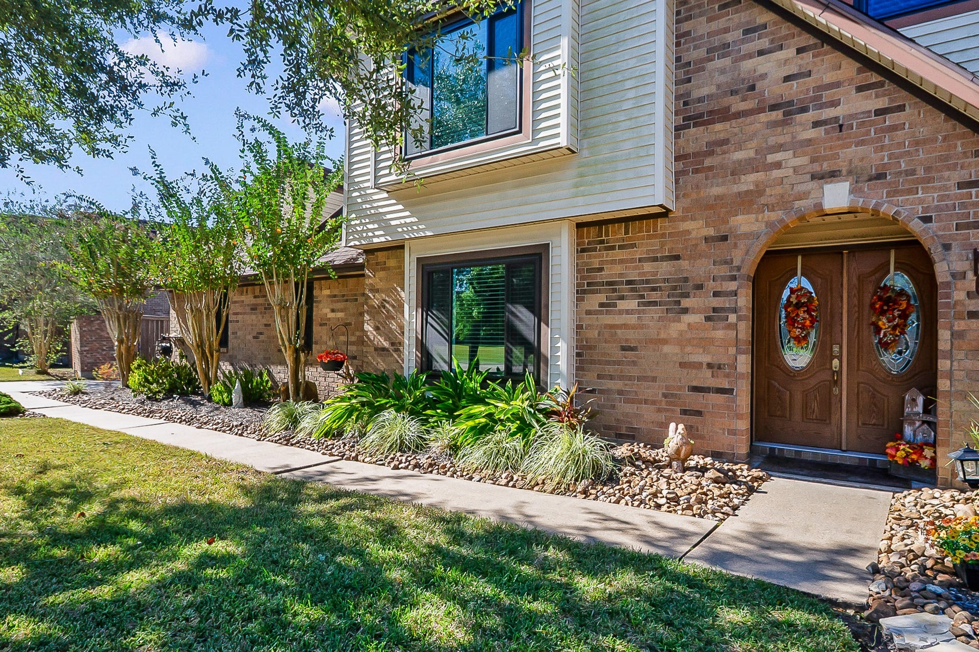 928 Oleander Street, Lake Jackson, TX 77566 Charming brick home with elegant arch-top double doors, lush landscaping, and a welcoming walkway.