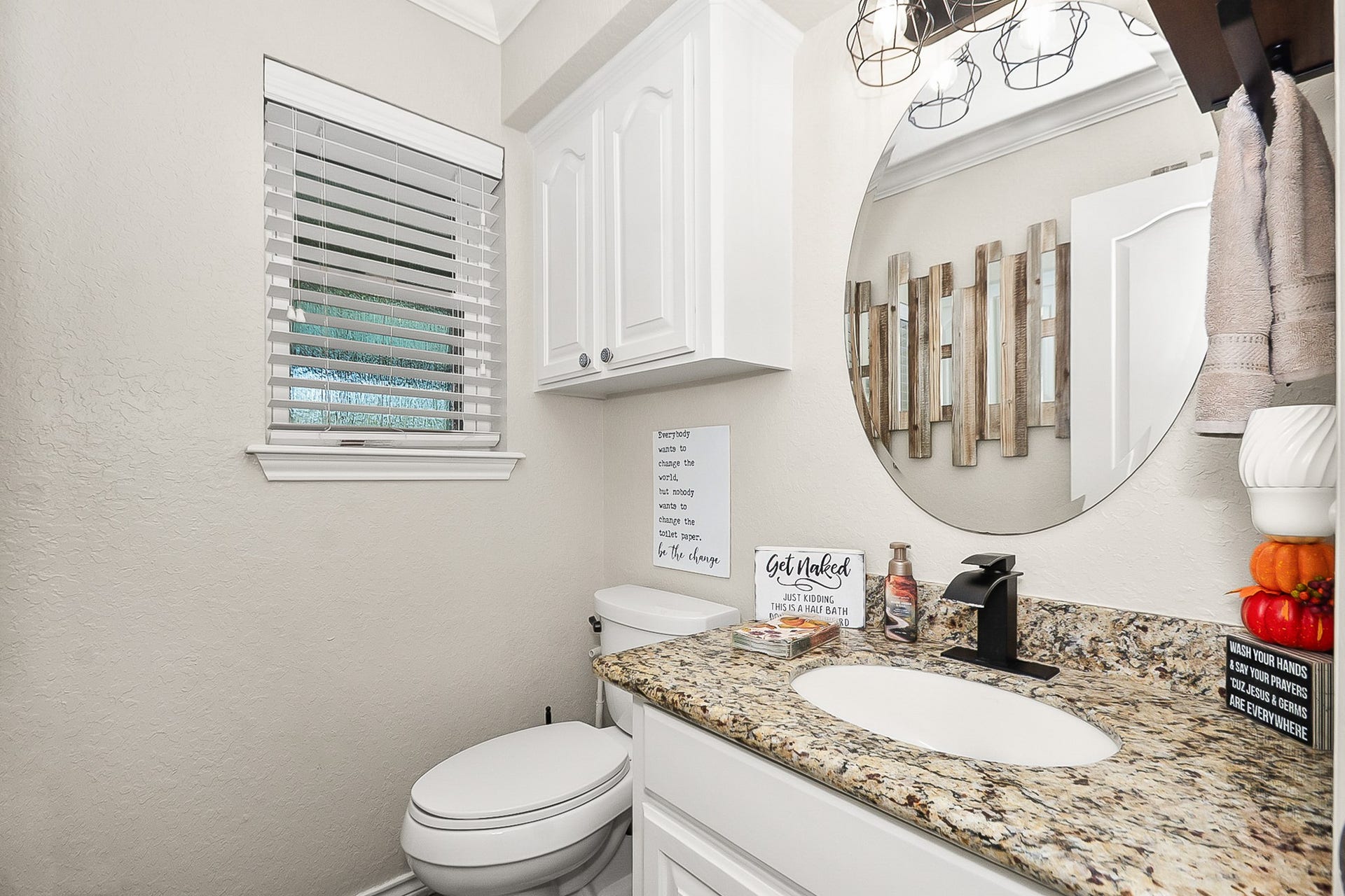 928 Oleander Street, Lake Jackson, TX 77566 Charming bathroom featuring a granite countertop, round mirror, and sleek black fixtures, enhanced by white cabinetry and a window for natural light.