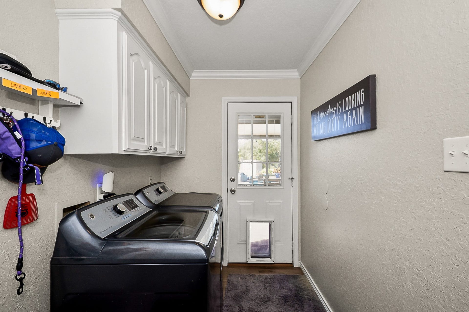 928 Oleander Street, Lake Jackson, TX 77566 Bright and functional laundry room featuring modern appliances, ample storage with overhead cabinets, and a convenient exterior door with glass paneling.