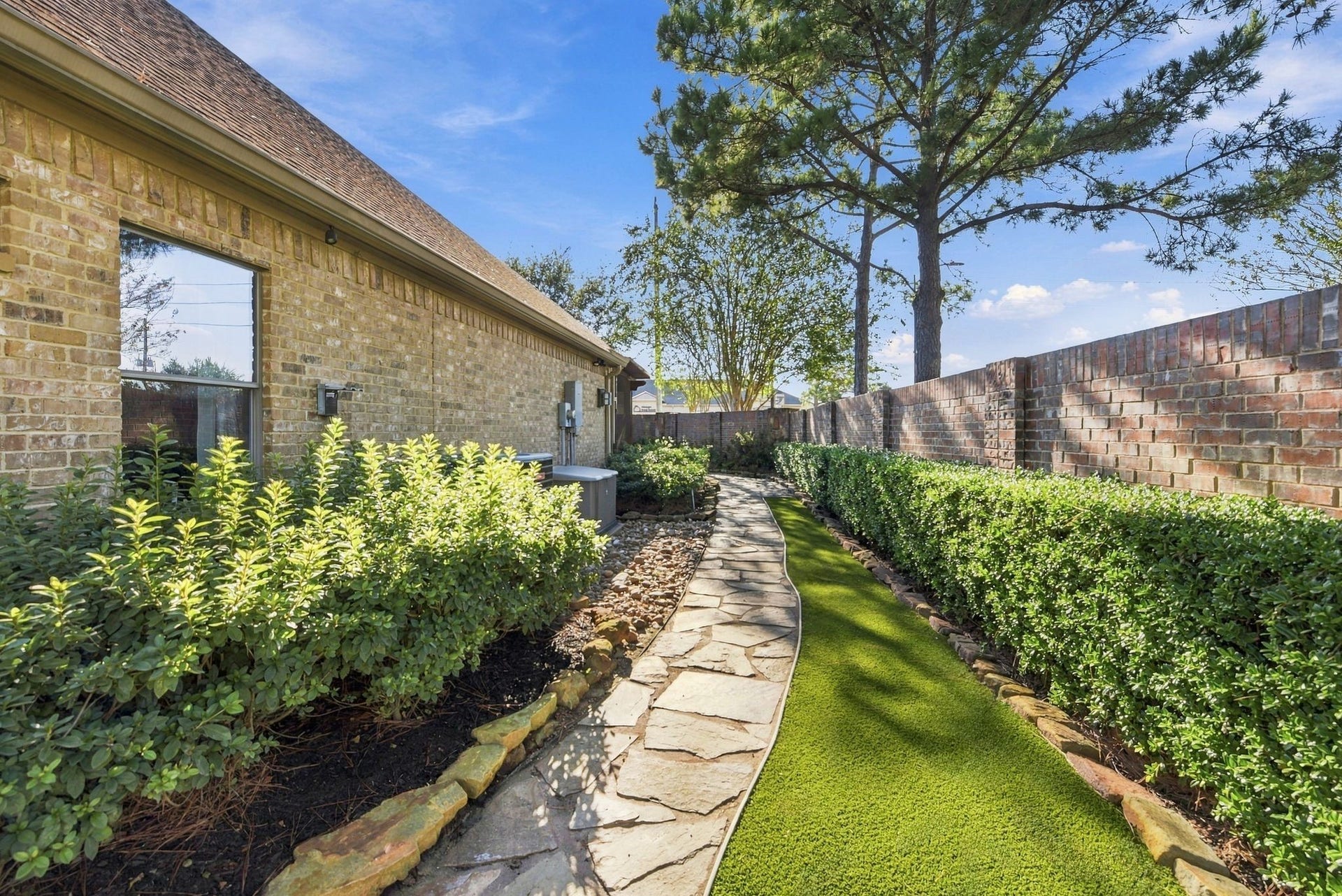 Garden pathway lined along the side of the home with lush greenery and a stone walkway.