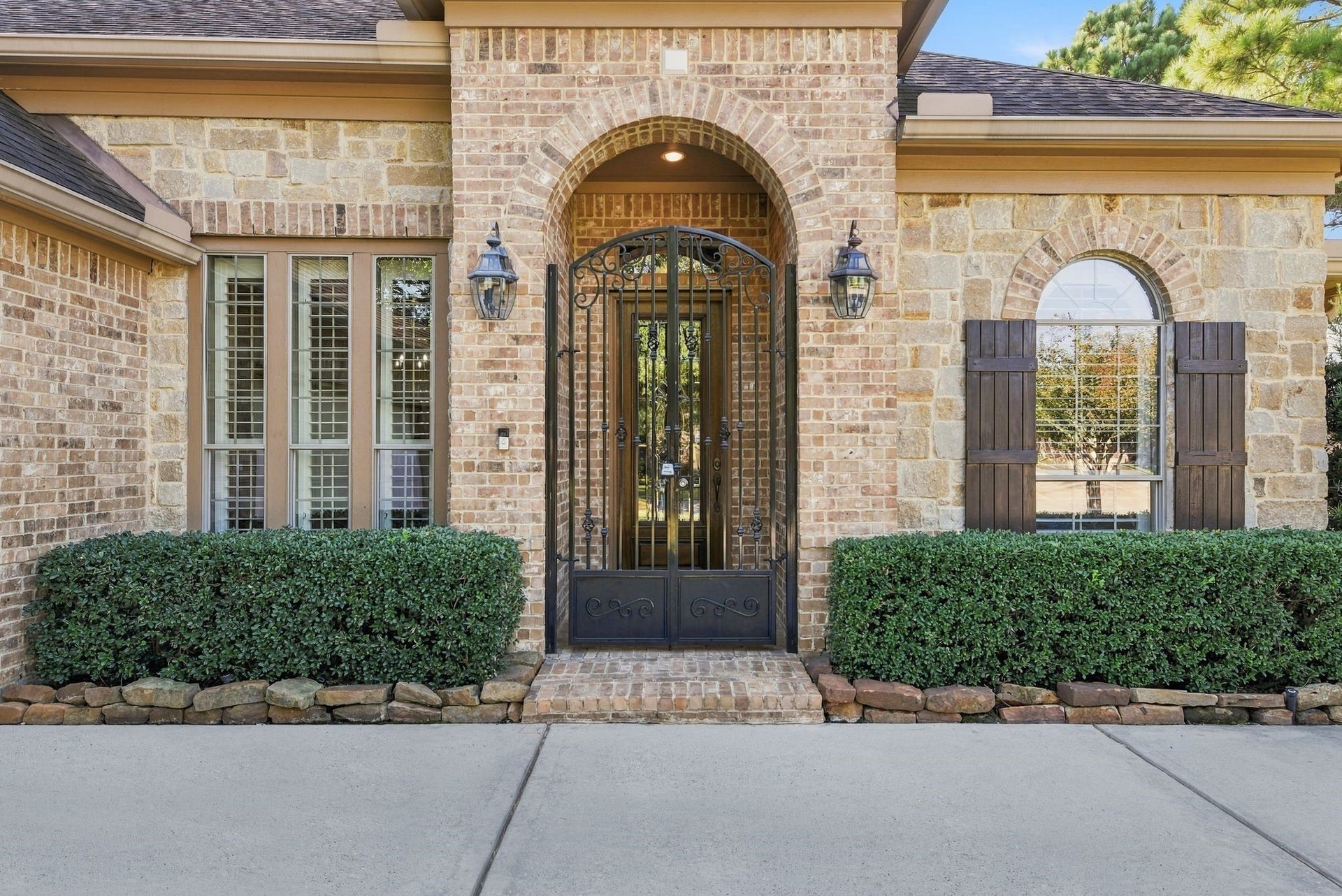 Gorgeous brick and stone exterior with elegant arched entryway and decorative wrought iron gate entry.