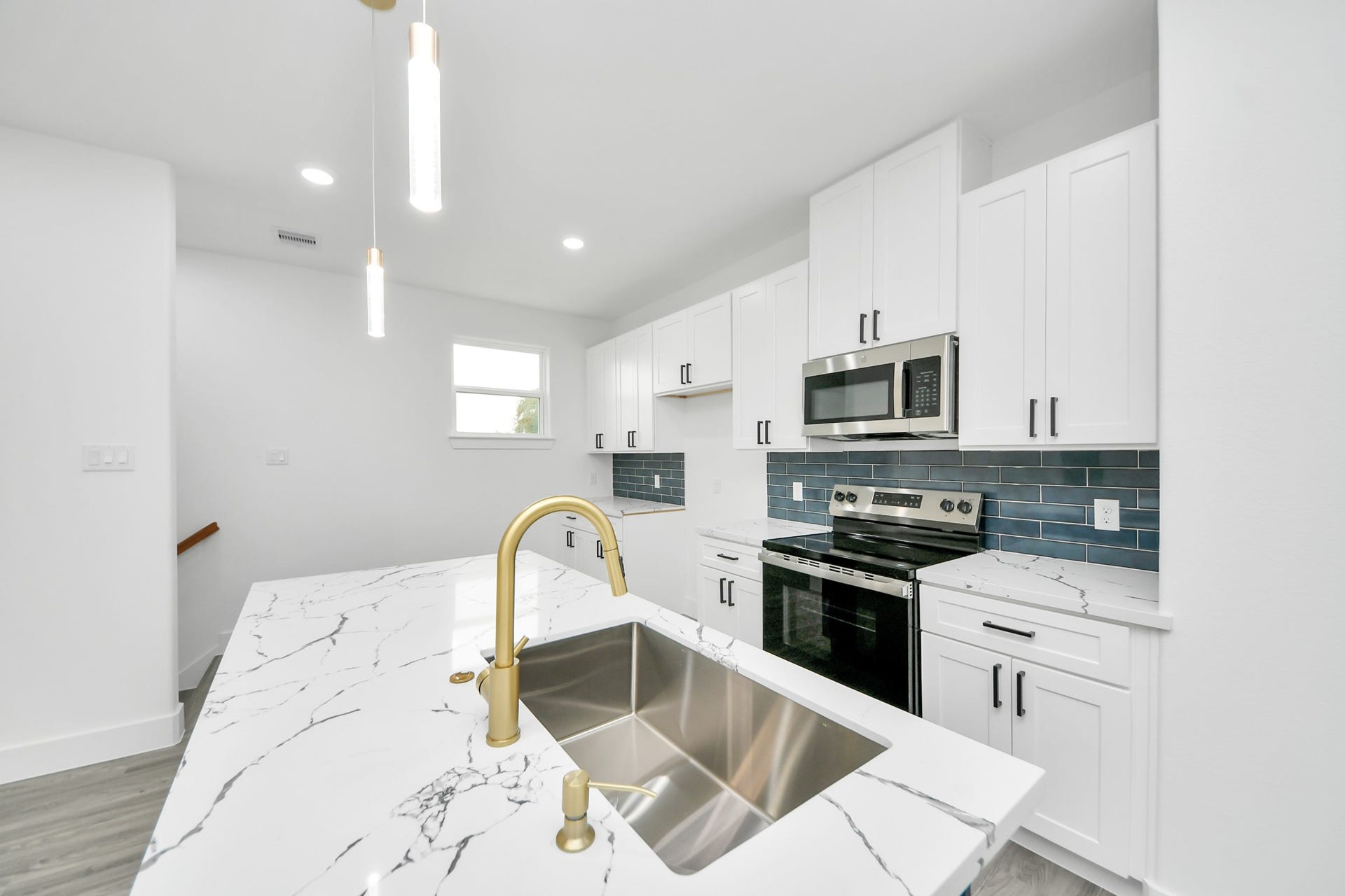 6707 Knox Street, Houston, TX 77091 Sleek modern kitchen featuring elegant white cabinetry, a striking marble countertop island with a gold faucet, and stainless steel appliances complemented by a stylish dark blue backsplash.