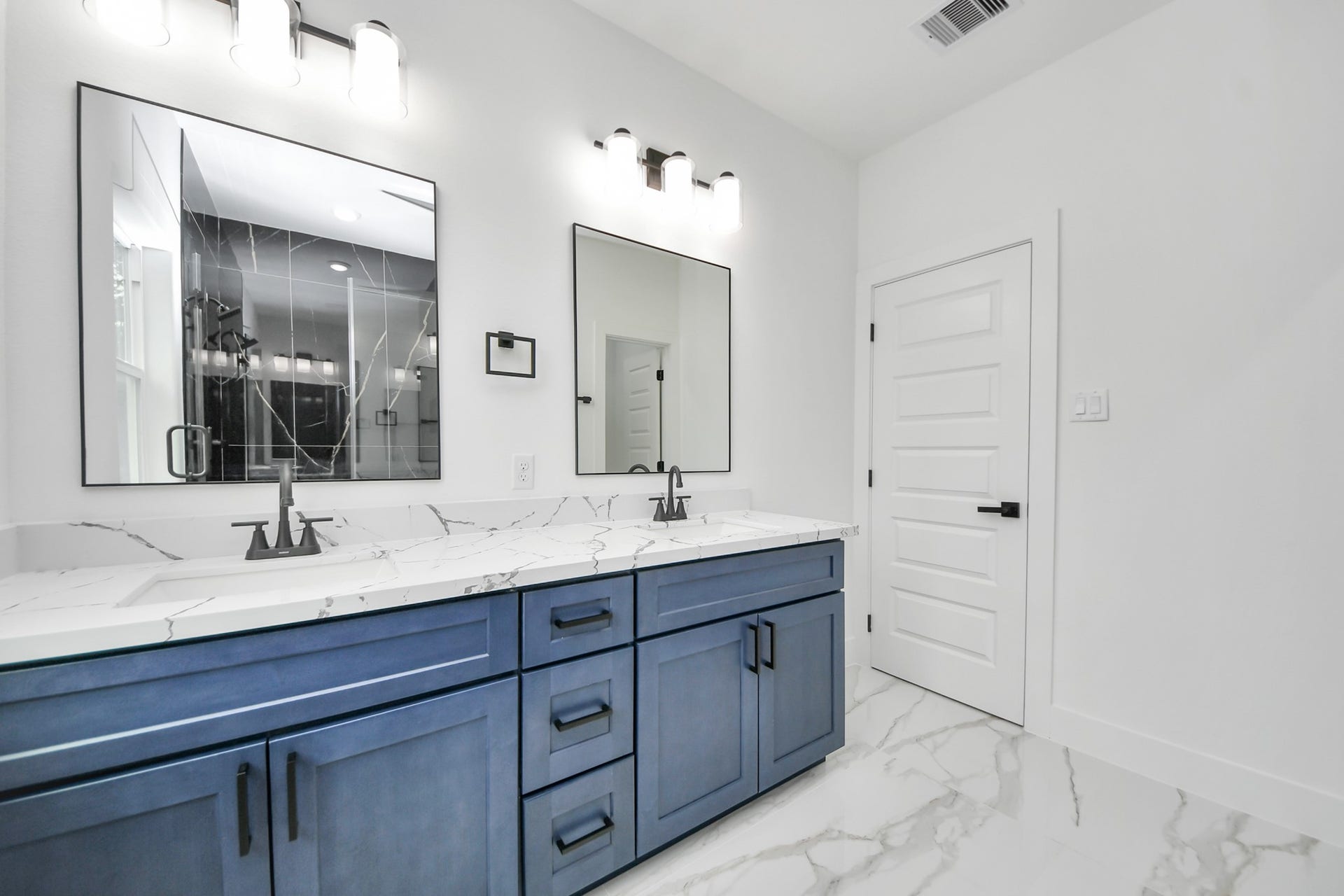 6707 Knox Street, Houston, TX 77091 Elegant bathroom featuring a double vanity with striking blue cabinetry, marble countertops, and modern fixtures, complemented by sleek mirrors and contemporary lighting.