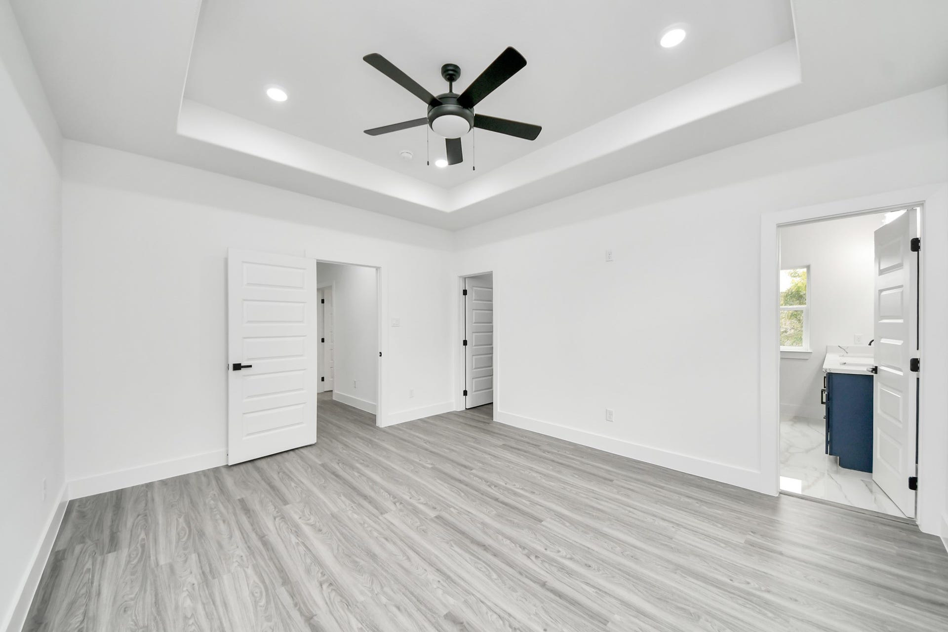 6707 Knox Street, Houston, TX 77091 Spacious bedroom featuring elegant tray ceilings, sleek wood flooring, and a modern ceiling fan, with convenient access to an en-suite bathroom.