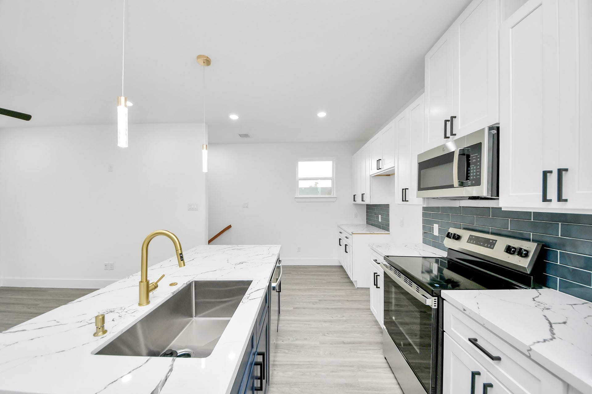 6707 Knox Street, Houston, TX 77091 Sleek modern kitchen with elegant white cabinetry, marble countertops, and a stylish gold faucet. Features include stainless steel appliances, a dark blue tile backsplash, and ample lighting for a bright, inviting space.
