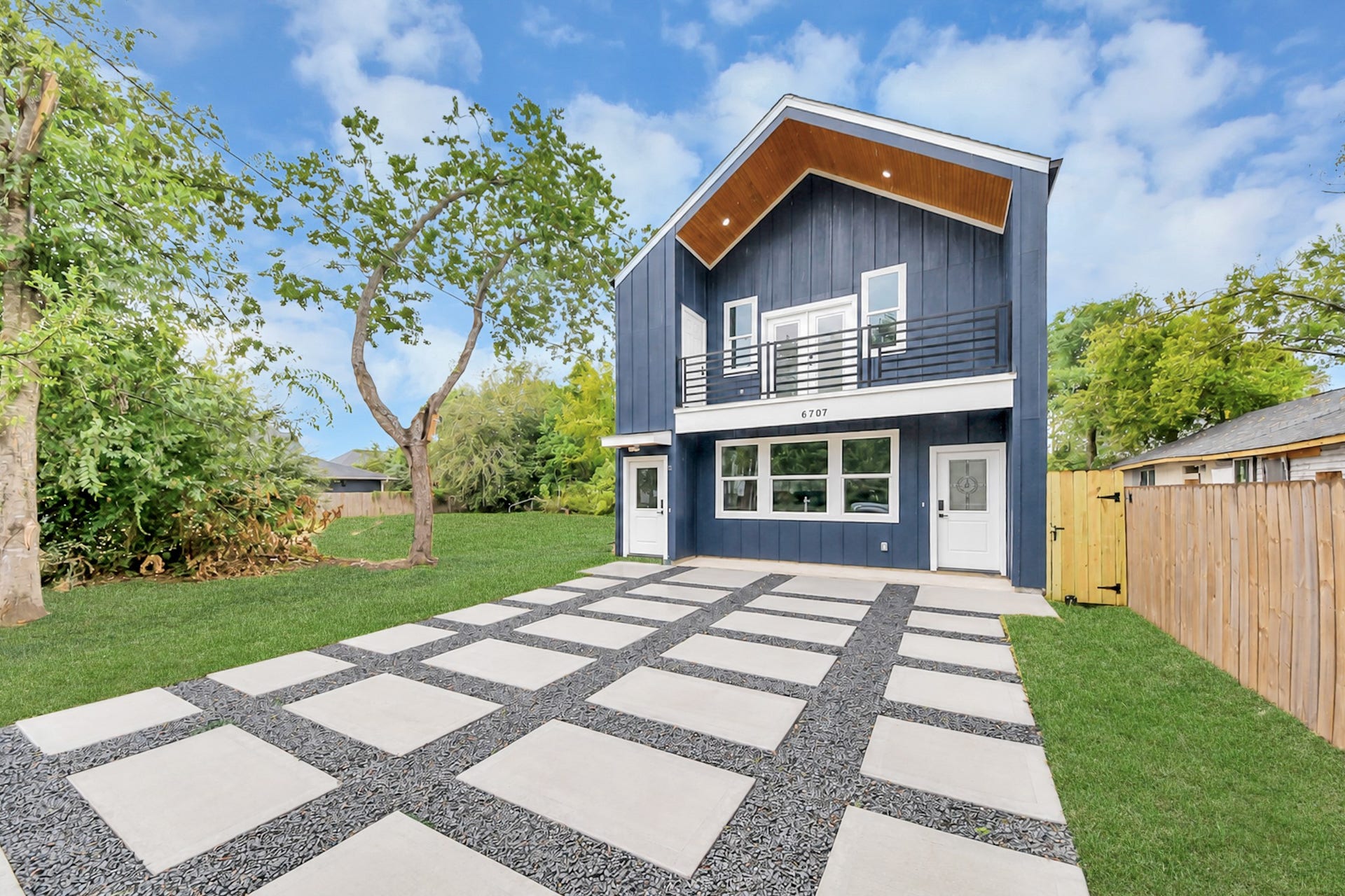 6707 Knox Street, Houston, TX 77091 Modern two-story home with striking blue exterior, large windows, and a sleek balcony. The spacious driveway features a stylish geometric design, and the lush lawn provides ample outdoor space.