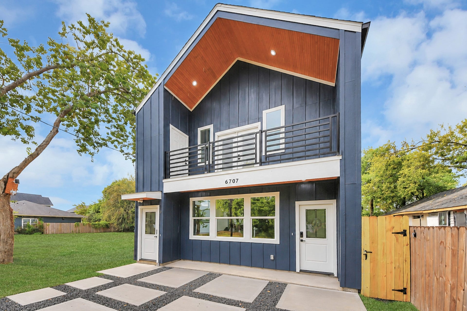 6707 Knox Street, Houston, TX 77091 Modern two-story home with striking navy blue siding, a sleek upper balcony, and a welcoming front porch, set in a spacious yard.