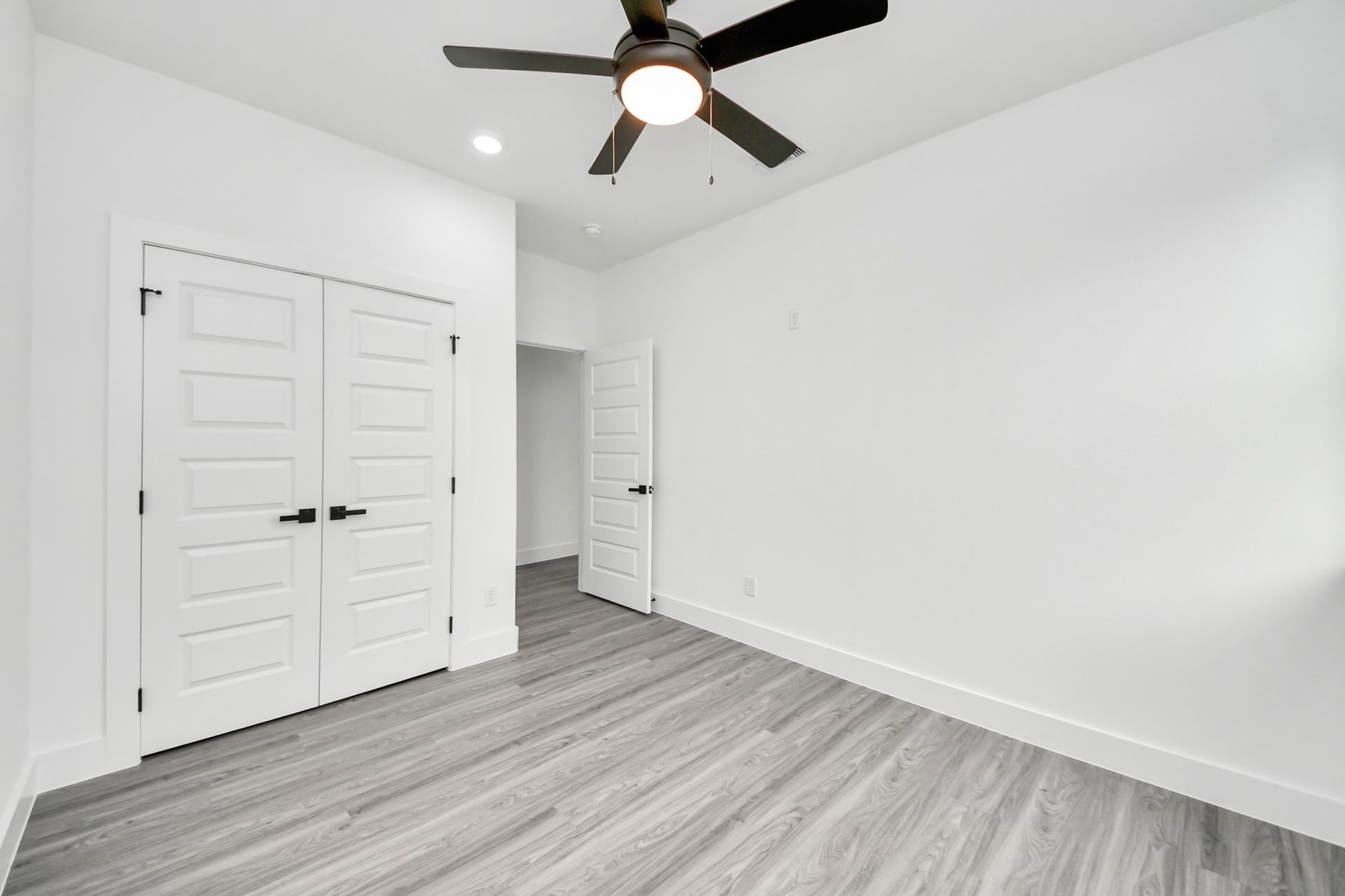 6707 Knox Street, Houston, TX 77091 Bright and spacious bedroom featuring sleek laminate flooring, a modern ceiling fan, and ample closet space with stylish white paneled doors.