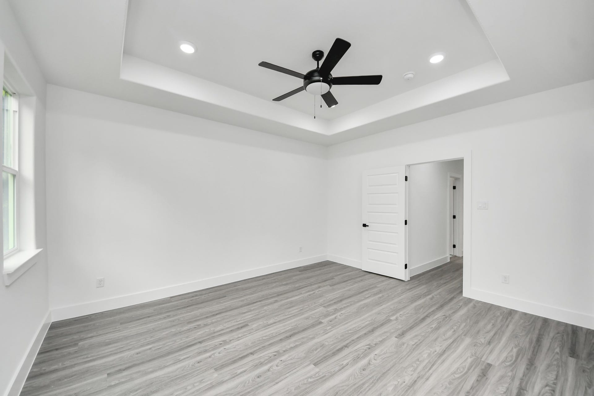 6707 Knox Street, Houston, TX 77091 Spacious room featuring elegant tray ceilings, sleek wood flooring, and ample natural light through large windows, complemented by modern recessed lighting and a ceiling fan.