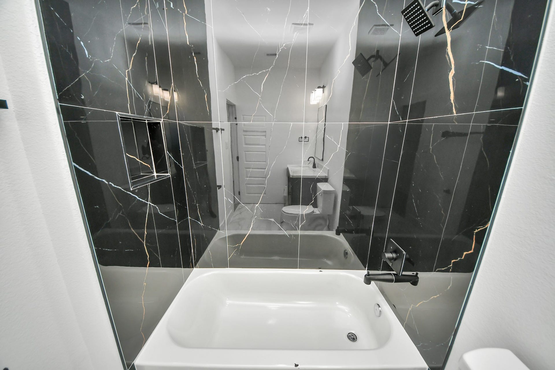 6707 Knox Street, Houston, TX 77091 Luxurious bathroom featuring a sleek black marble shower wall with elegant veining, complemented by modern fixtures and a spacious white tub for ultimate relaxation.