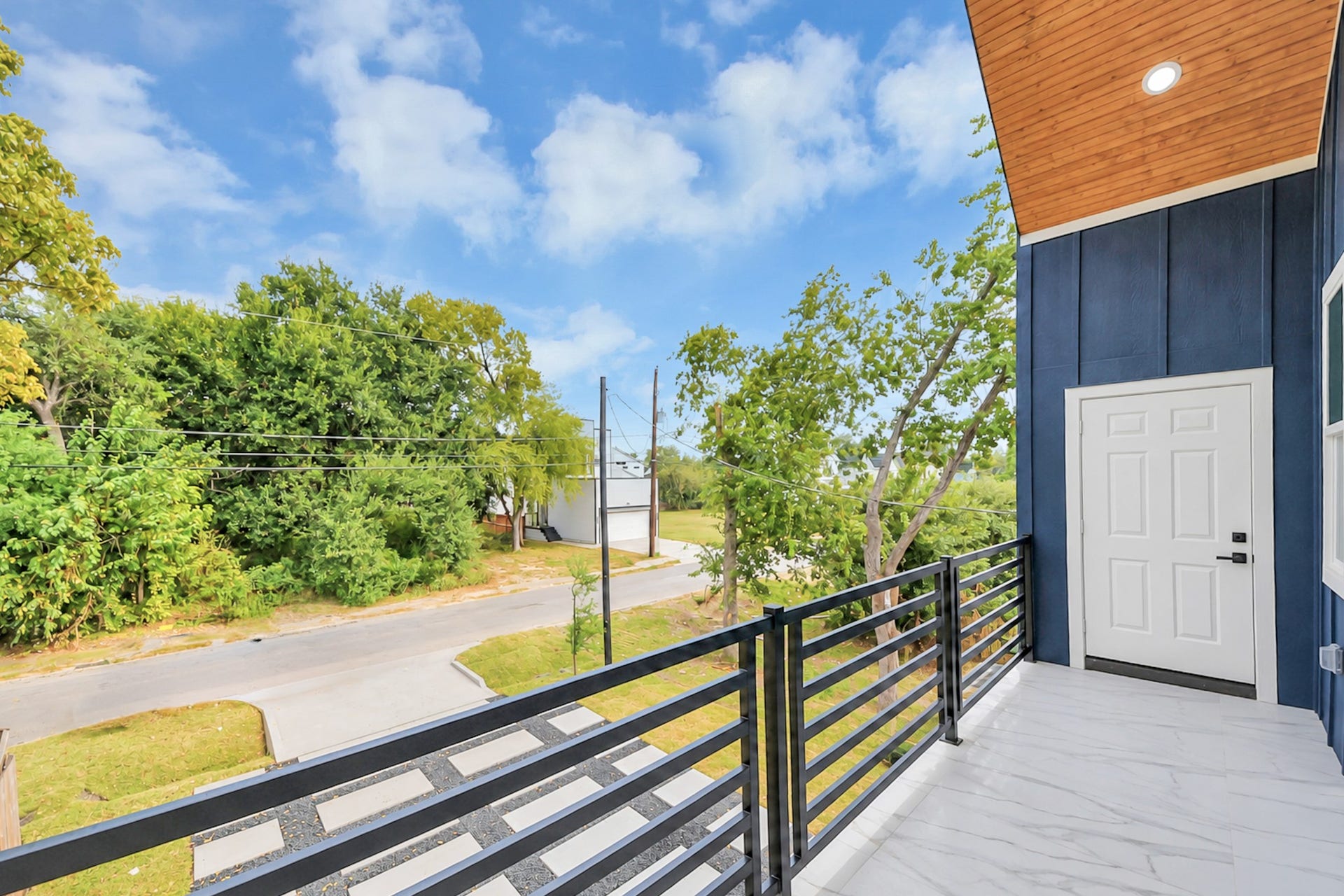 6707 Knox Street, Houston, TX 77091 Charming balcony with sleek railing offers a serene view of lush greenery and a quiet street, perfect for relaxation.