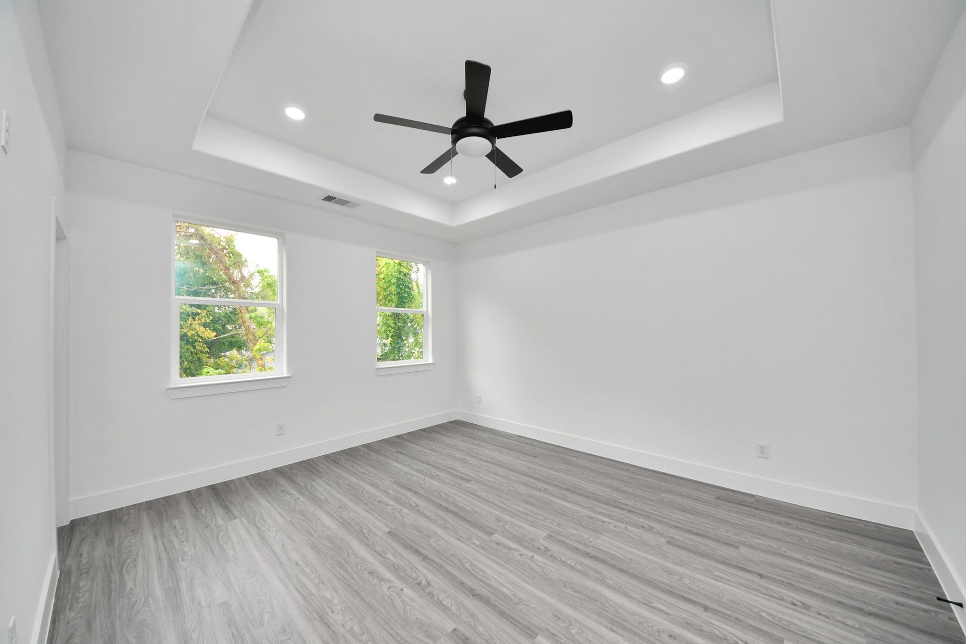 6707 Knox Street, Houston, TX 77091 Spacious, light-filled room featuring elegant wood flooring, a stylish tray ceiling with recessed lighting, and a modern ceiling fan, offering a serene and comfortable atmosphere.