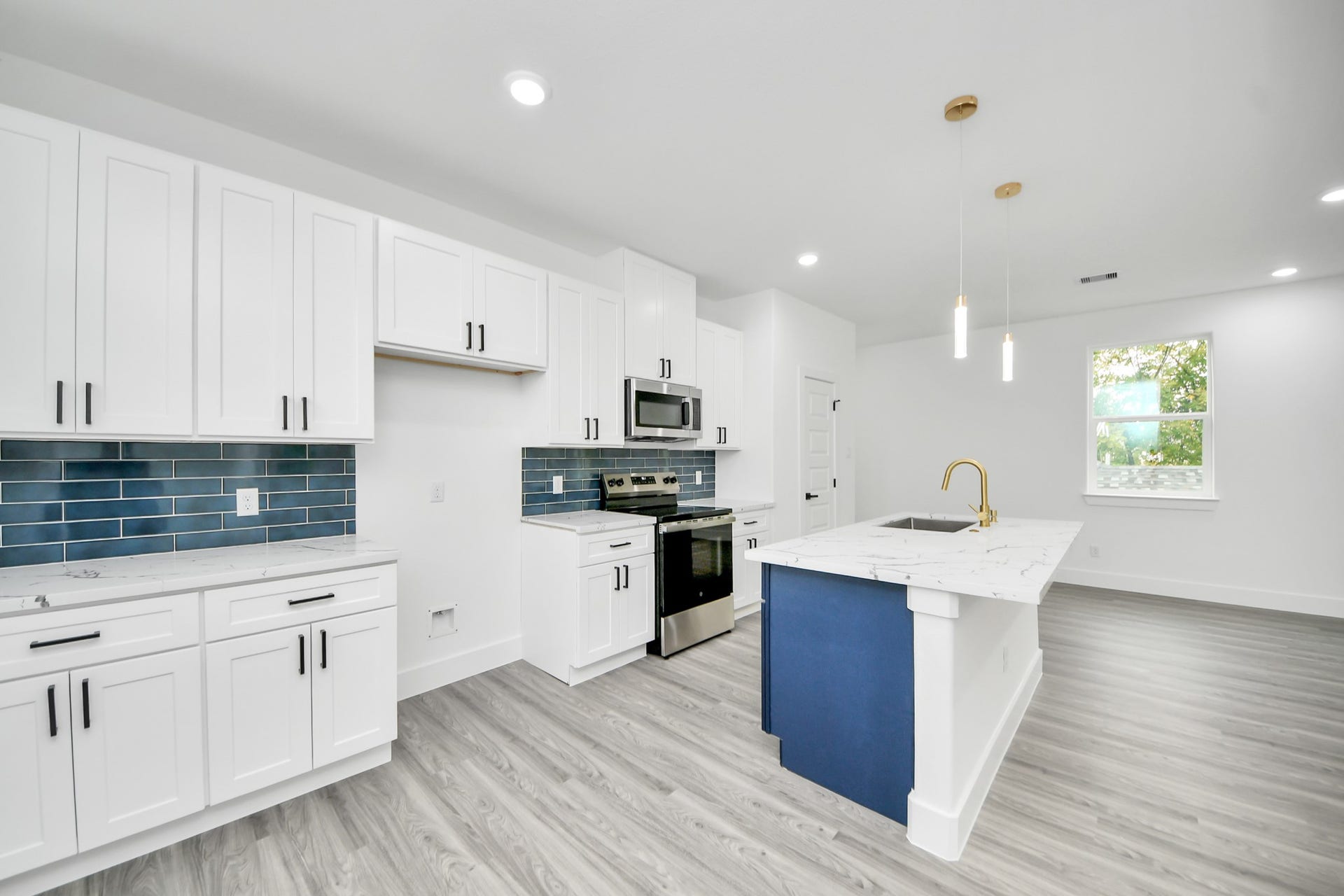 6707 Knox Street, Houston, TX 77091 Sleek modern kitchen featuring white cabinetry, stainless steel appliances, and a chic blue tile backsplash. The spacious island with a marble countertop and stylish pendant lighting enhances the contemporary design.