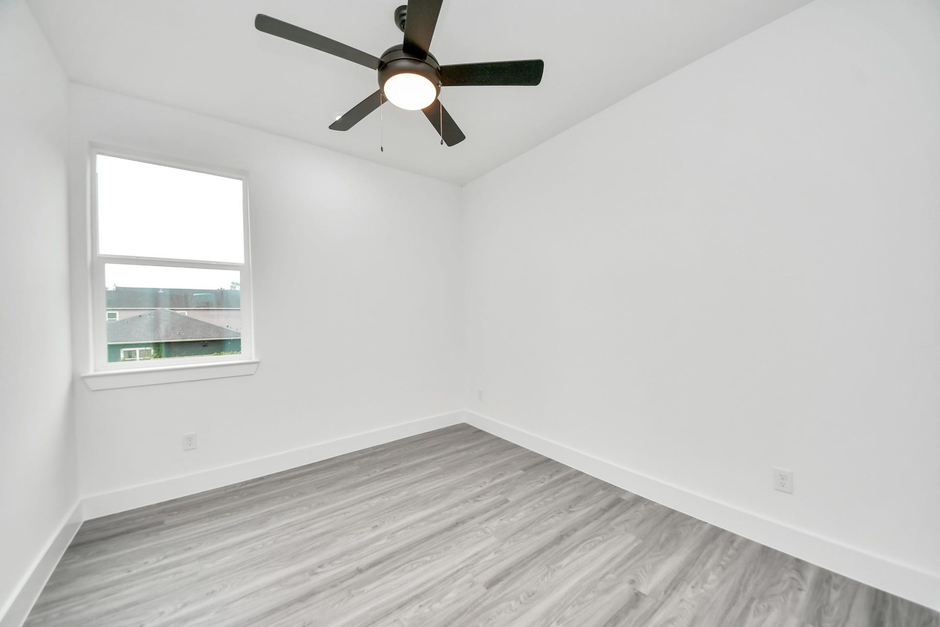 6707 Knox Street, Houston, TX 77091 Bright and airy room featuring sleek gray flooring, a modern ceiling fan, and a large window for natural light.