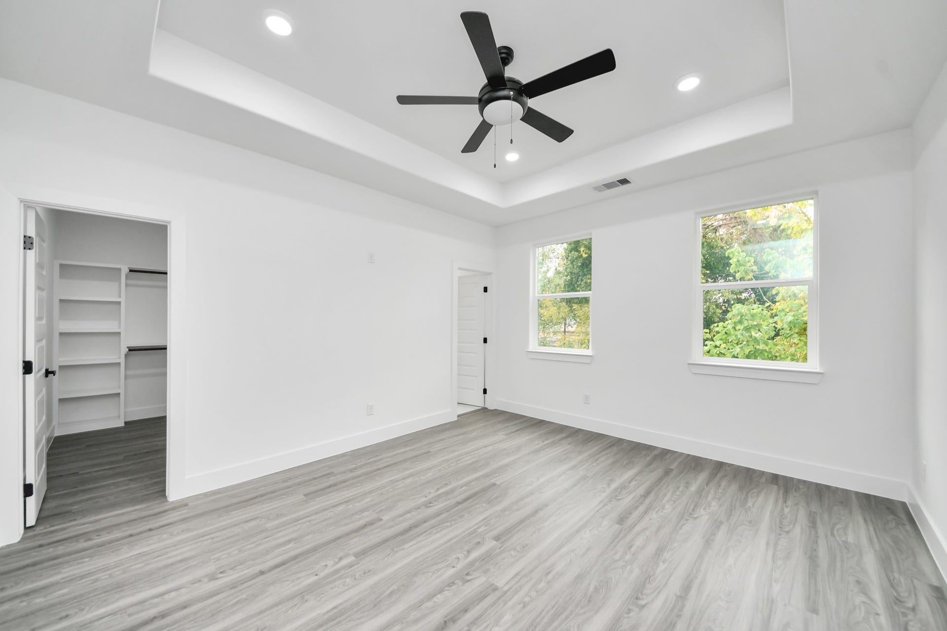 6707 Knox Street, Houston, TX 77091 Bright and spacious bedroom featuring a stylish tray ceiling, modern ceiling fan, and large windows that offer abundant natural light. The room includes sleek wood flooring and a generous walk-in closet for ample storage.