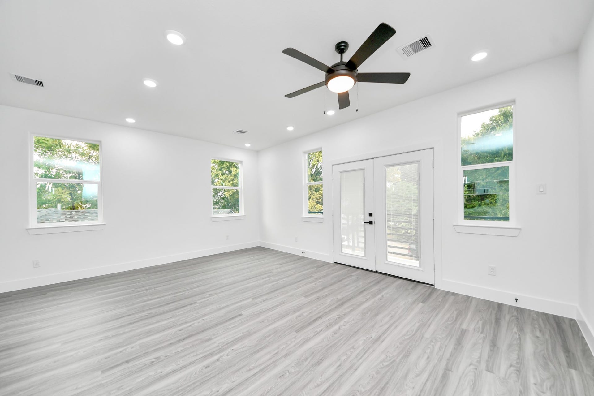 6707 Knox Street, Houston, TX 77091 Spacious and bright room featuring sleek wood flooring, French doors leading to an outdoor space, and modern recessed lighting, complemented by a contemporary ceiling fan.
