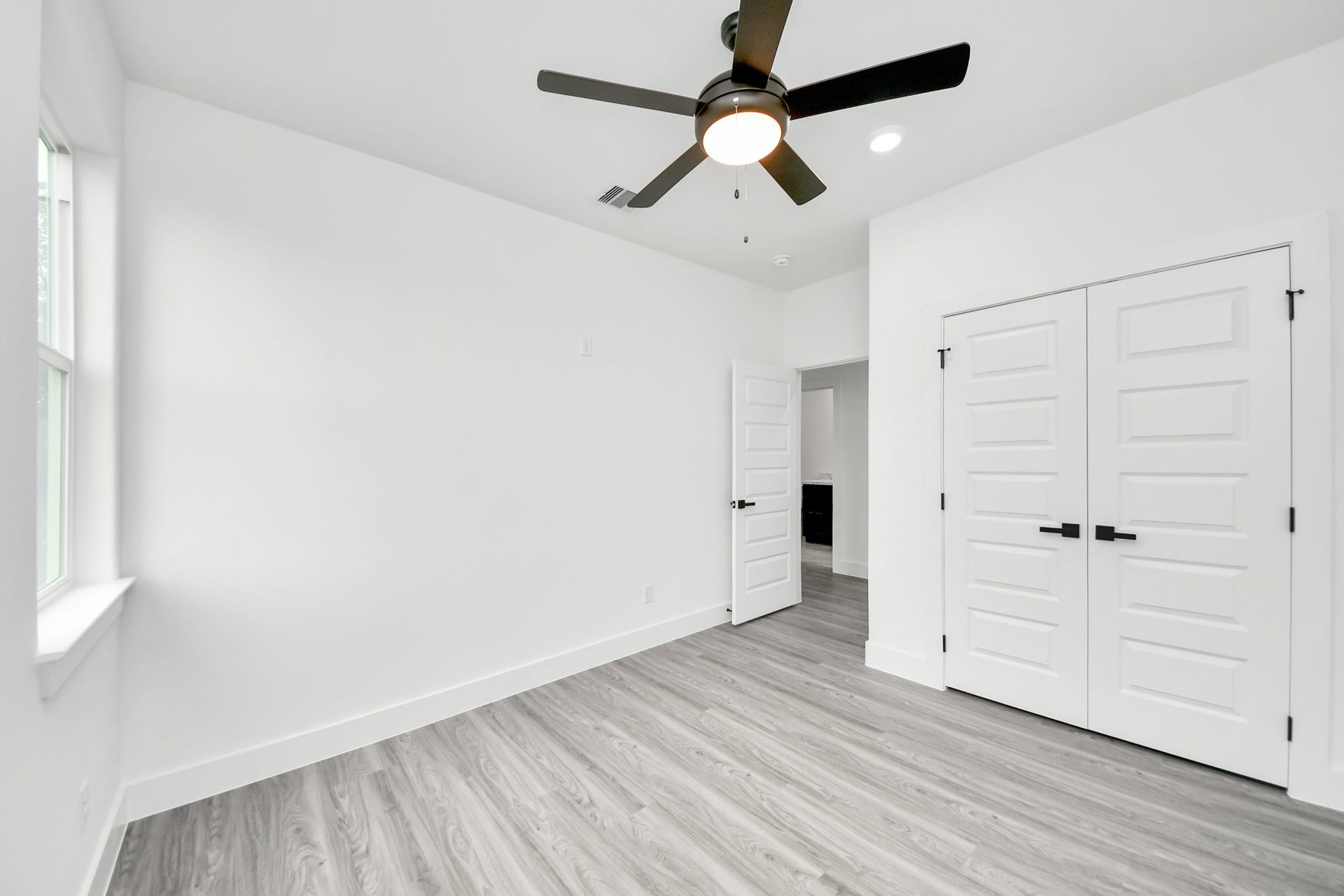 6707 Knox Street, Houston, TX 77091 Bright and spacious room featuring sleek wood flooring, a modern ceiling fan, and ample natural light, complemented by crisp white walls and stylish double doors.