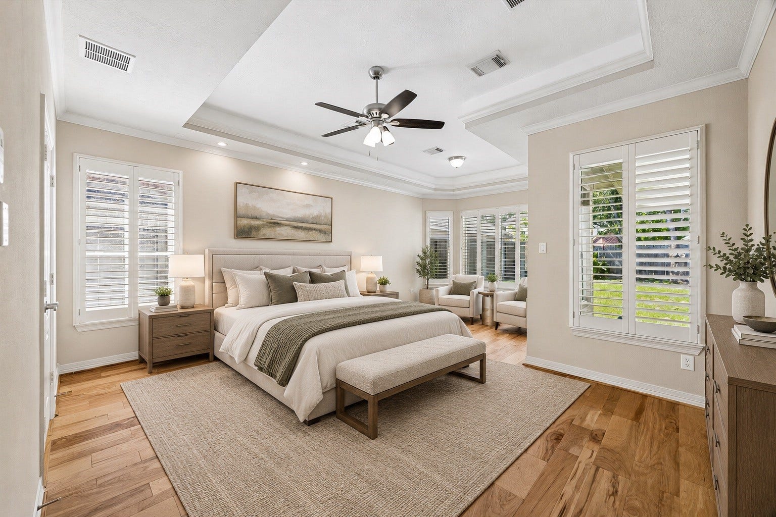 The light-filled first floor primary suite is relaxing, and features an elegant tray ceiling, plantation shutters & warm wood look floors. Photo virtually staged.