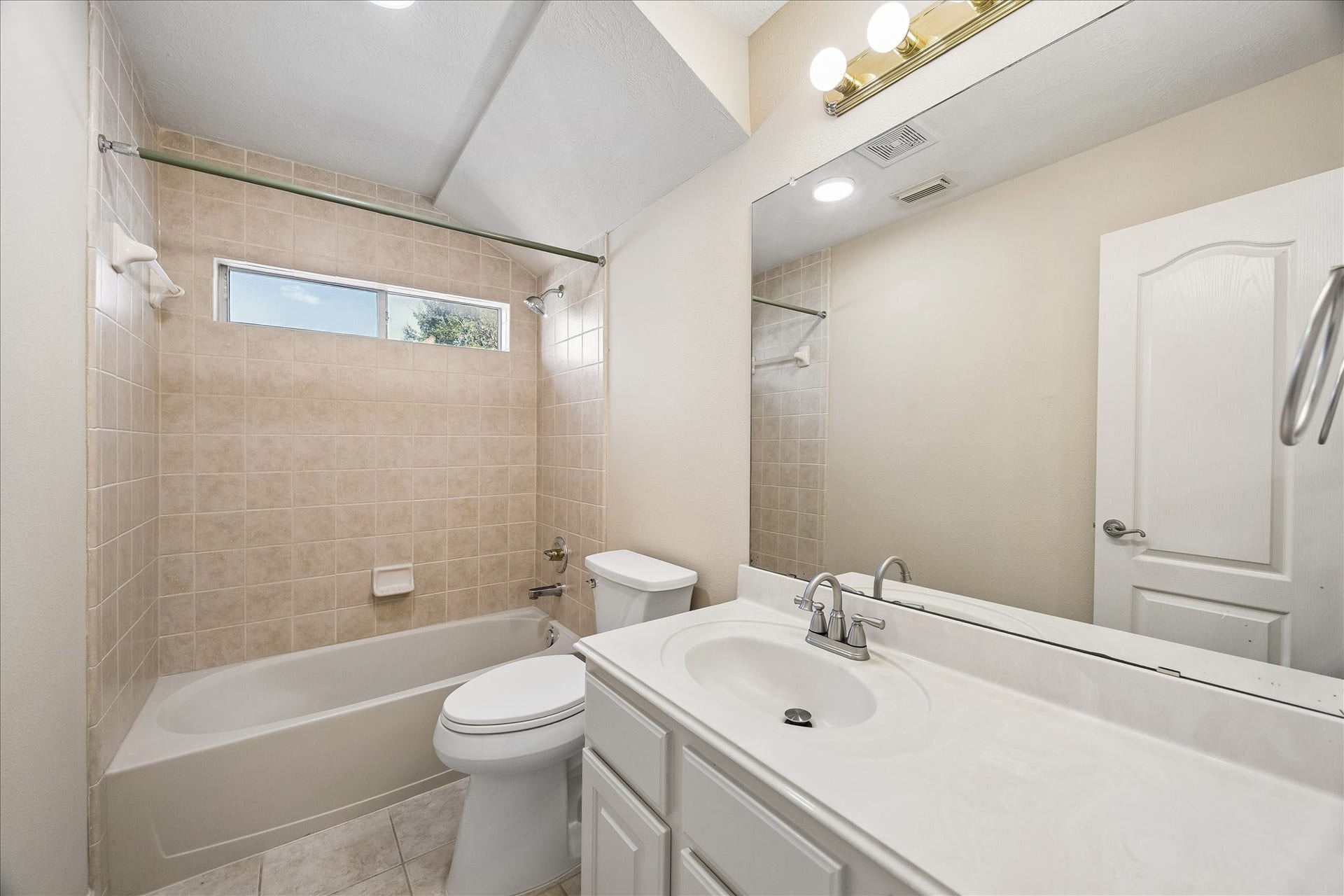 Secondary bath with vaulted ceiling, solid surface counters and storage space.