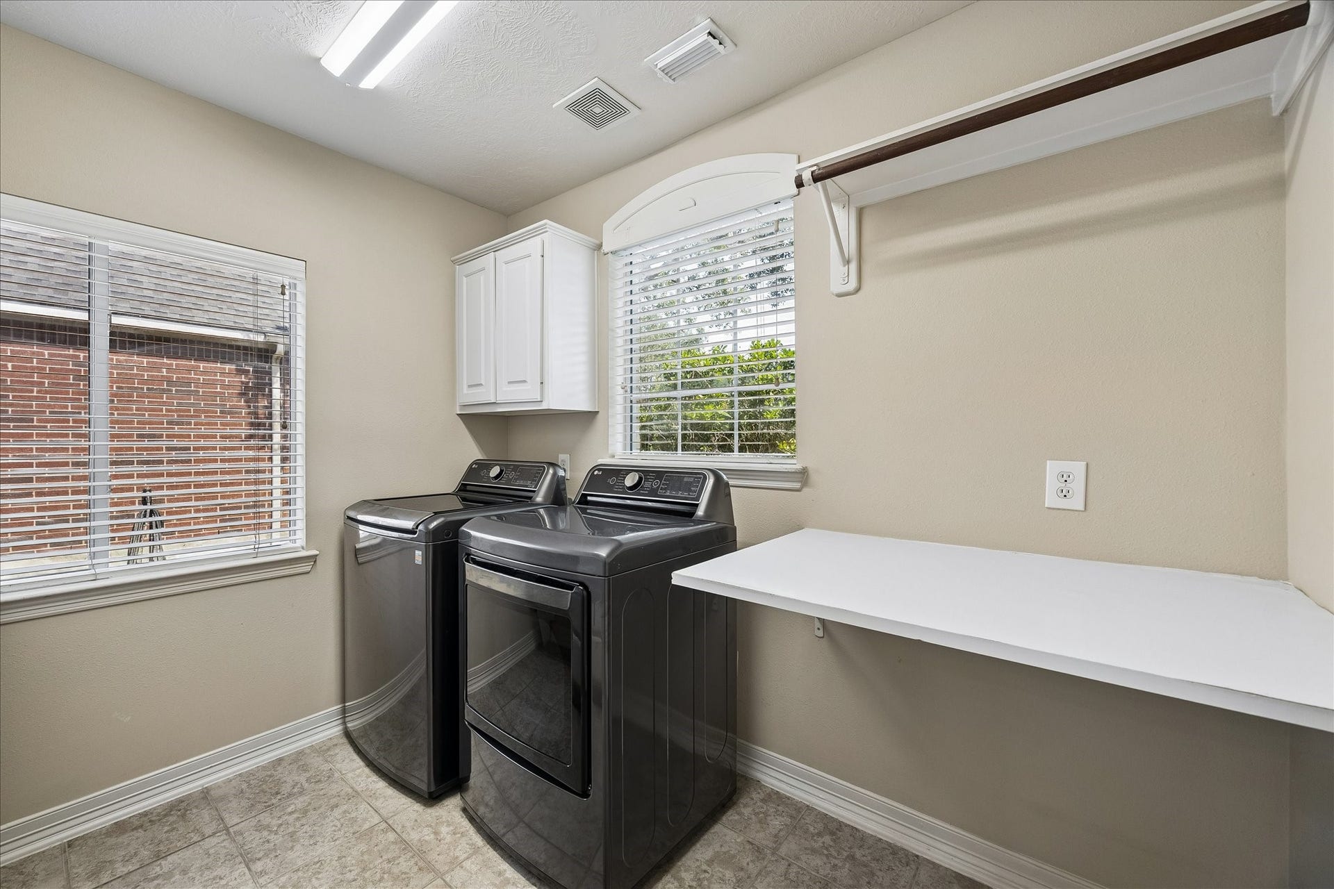 The downstairs laundry room offers ample space and a bright, functional setting with a folding table and hanging rack.