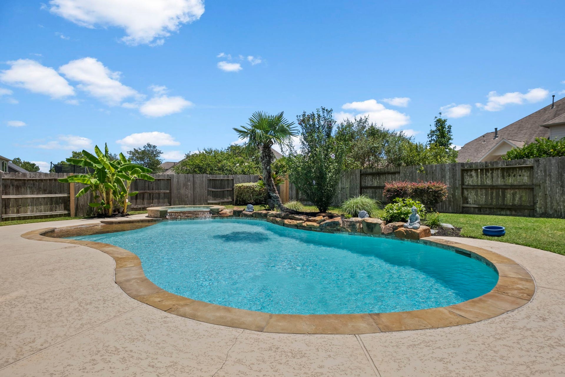 19519 Arbor Lodge Drive, Cypress, TX 77433 This backyard features a beautifully landscaped pool with a rock waterfall, surrounded by lush greenery and a privacy fence, creating a private oasis perfect for relaxation.