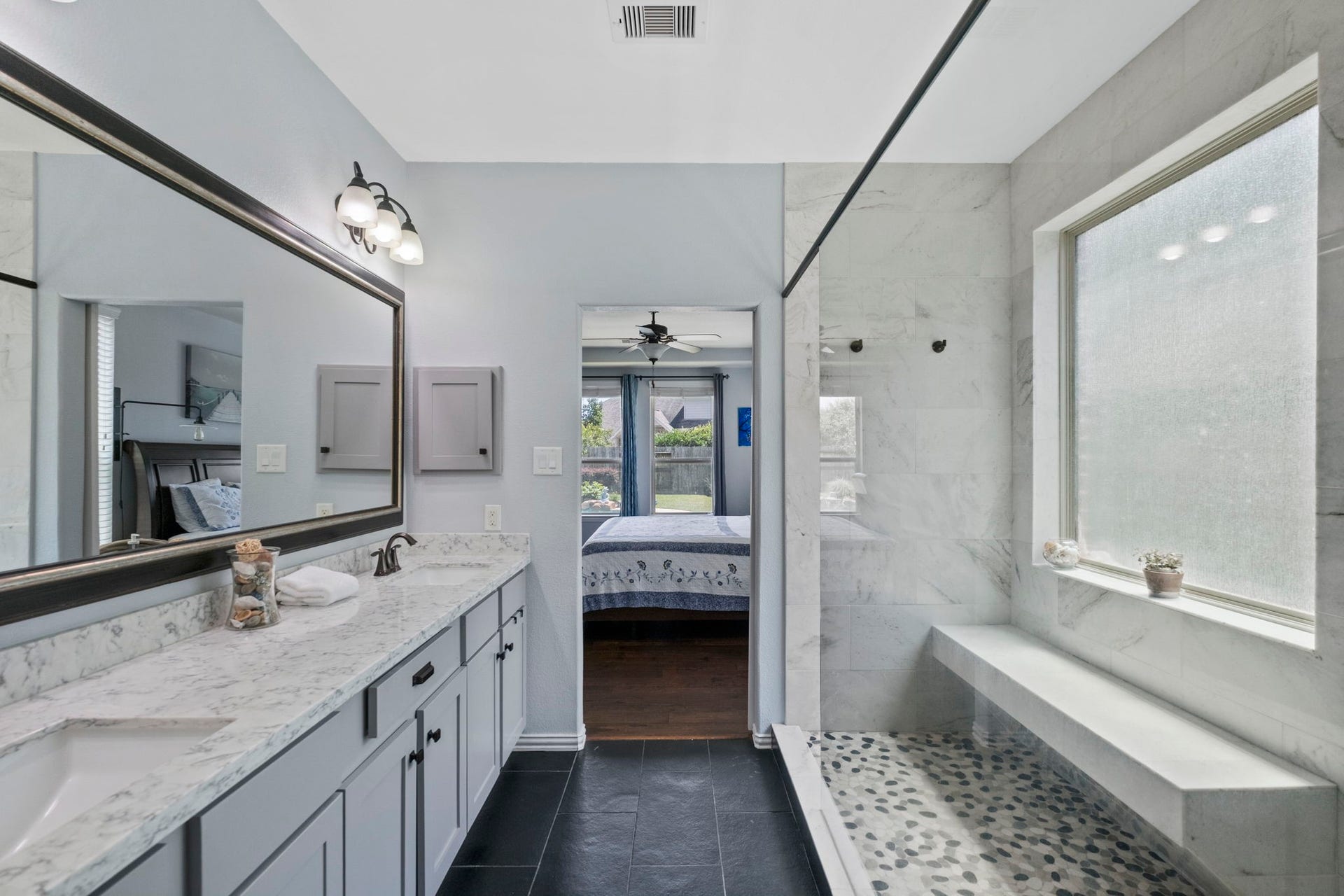 19519 Arbor Lodge Drive, Cypress, TX 77433 This modern bathroom features a spacious shower with a pebble floor and a built-in bench, a large vanity with dual sinks and quartz countertops, and ample natural light, creating a bright and peaceful space.