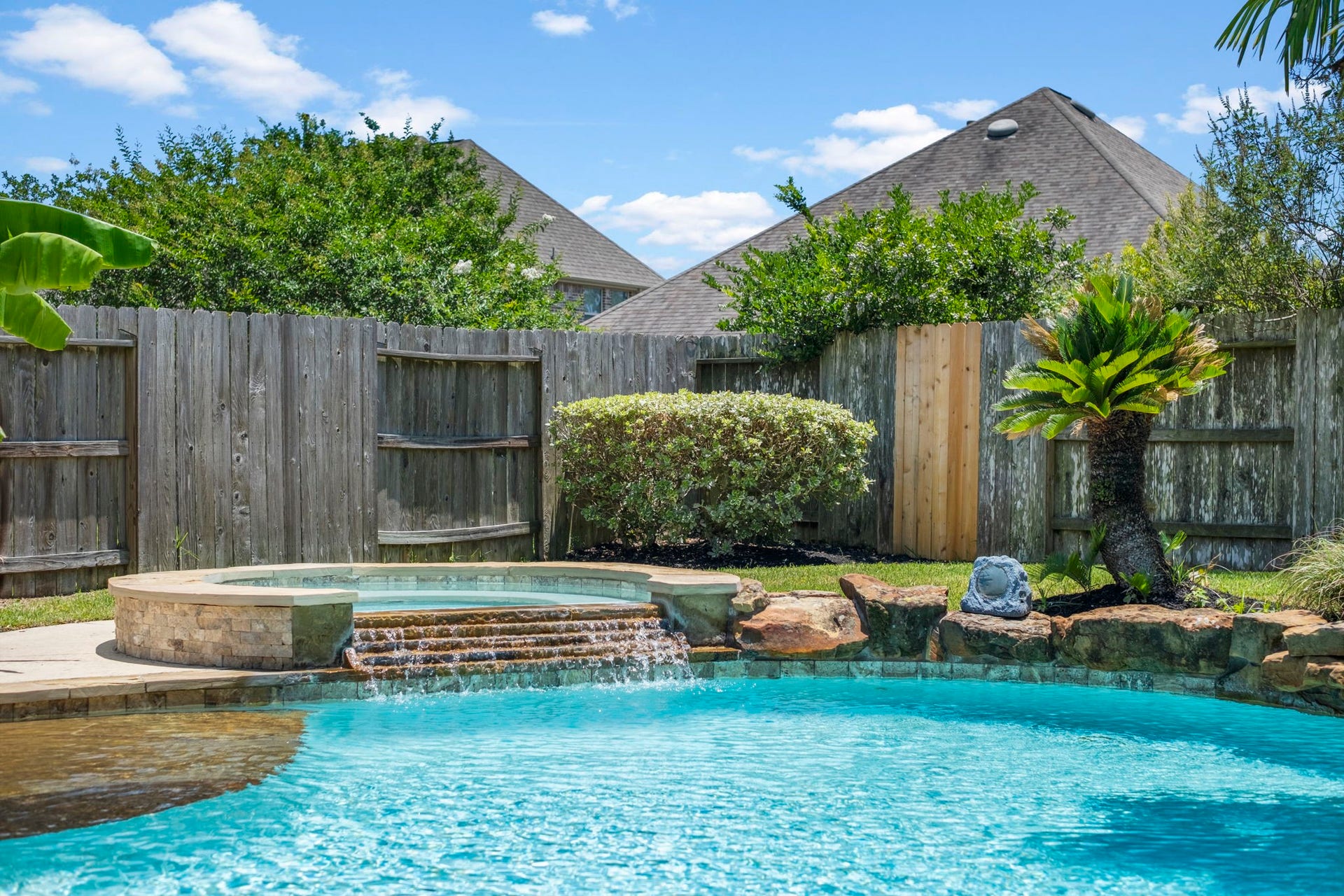 19519 Arbor Lodge Drive, Cypress, TX 77433 This backyard oasis features a sparkling pool with a connected hot tub, framed by lush greenery, perfect for relaxation and entertaining.