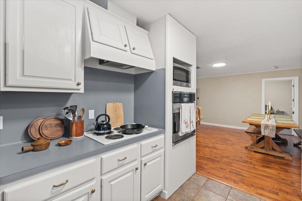 1209 E Brown Lane, Deer Park, TX 77536 Charming kitchen featuring sleek gray countertops, white cabinetry, built in oven and cooktop, leading gracefully into a cozy flex family/dining area with warm hardwood floors.