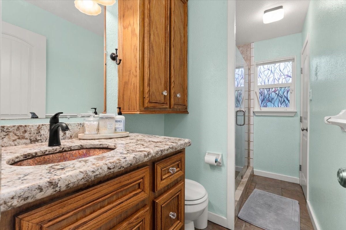 1209 E Brown Lane, Deer Park, TX 77536 Charming bathroom with a granite countertop and warm wooden cabinetry, featuring a walk-in shower with decorative glass windows. Hollywood style bath