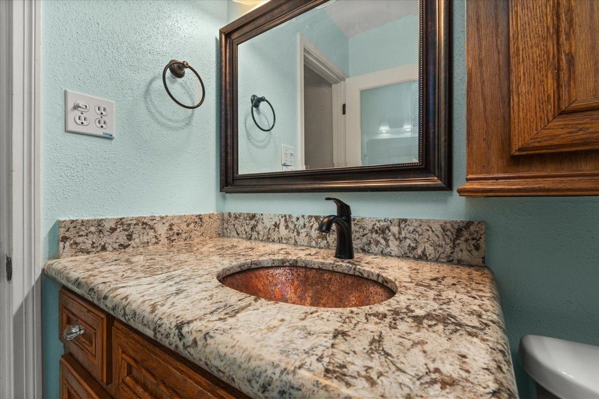 1209 E Brown Lane, Deer Park, TX 77536 Elegant bathroom vanity featuring a granite countertop, a stylish undermount sink, and a framed mirror, complemented by rich wooden cabinetry. Hollywood bath