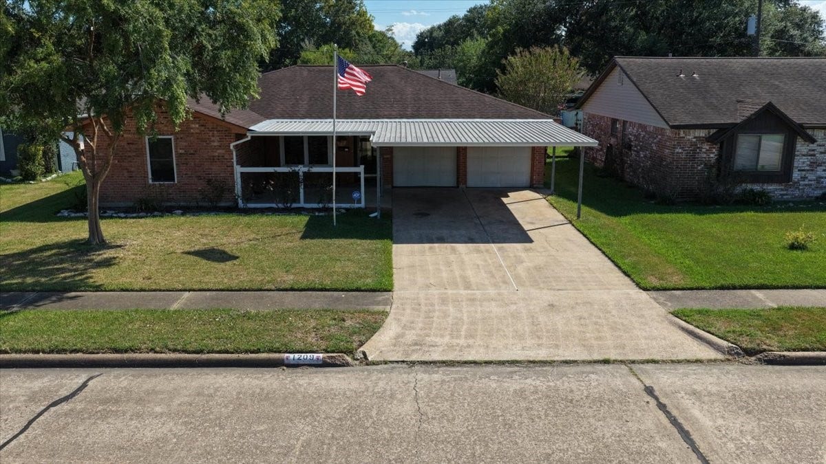 1209 E Brown Lane, Deer Park, TX 77536 Charming brick home with a welcoming front porch, spacious driveway, and attached two-car garage with carport, set on a well-maintained lot with mature trees.