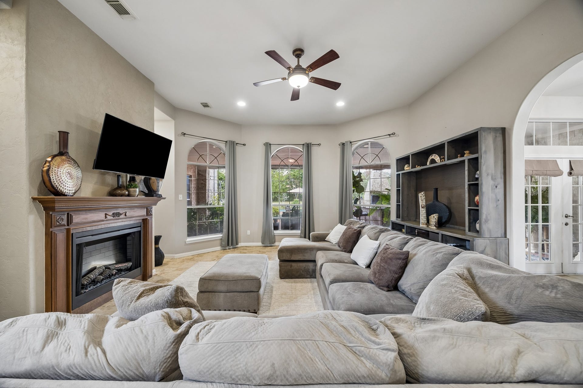 1319 Brazoswood Place, Richmond, TX 77406 Refined yet inviting, this spacious living area pairs architectural windows and a classic fireplace with backyard pool and patio views.