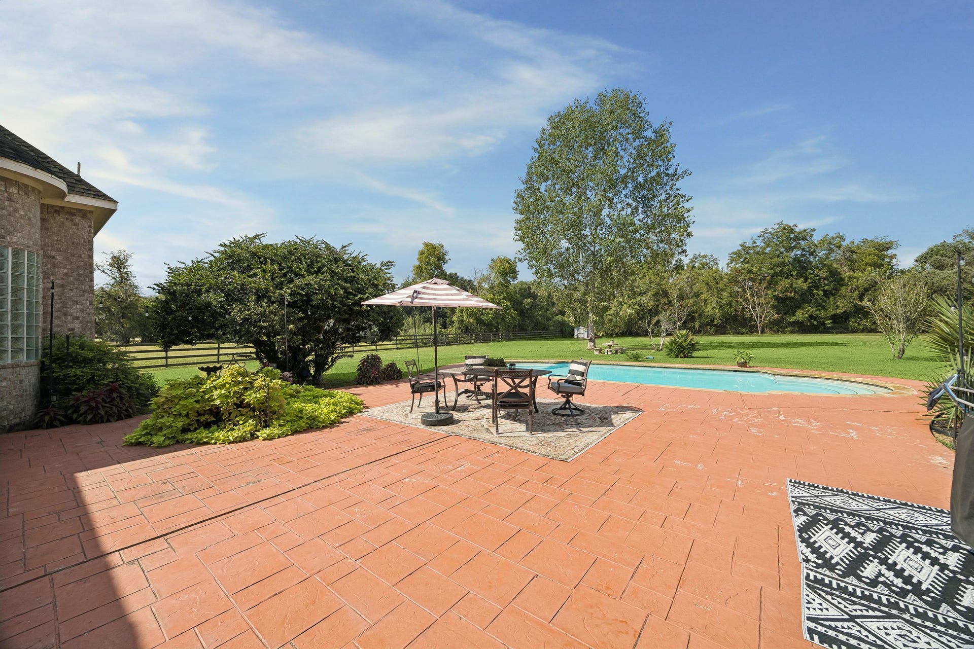 1319 Brazoswood Place, Richmond, TX 77406 A private backyard oasis features a sparkling pool with wide entry steps, expansive sun-drenched decking, and a spacious covered patio ideal for relaxing and entertaining.