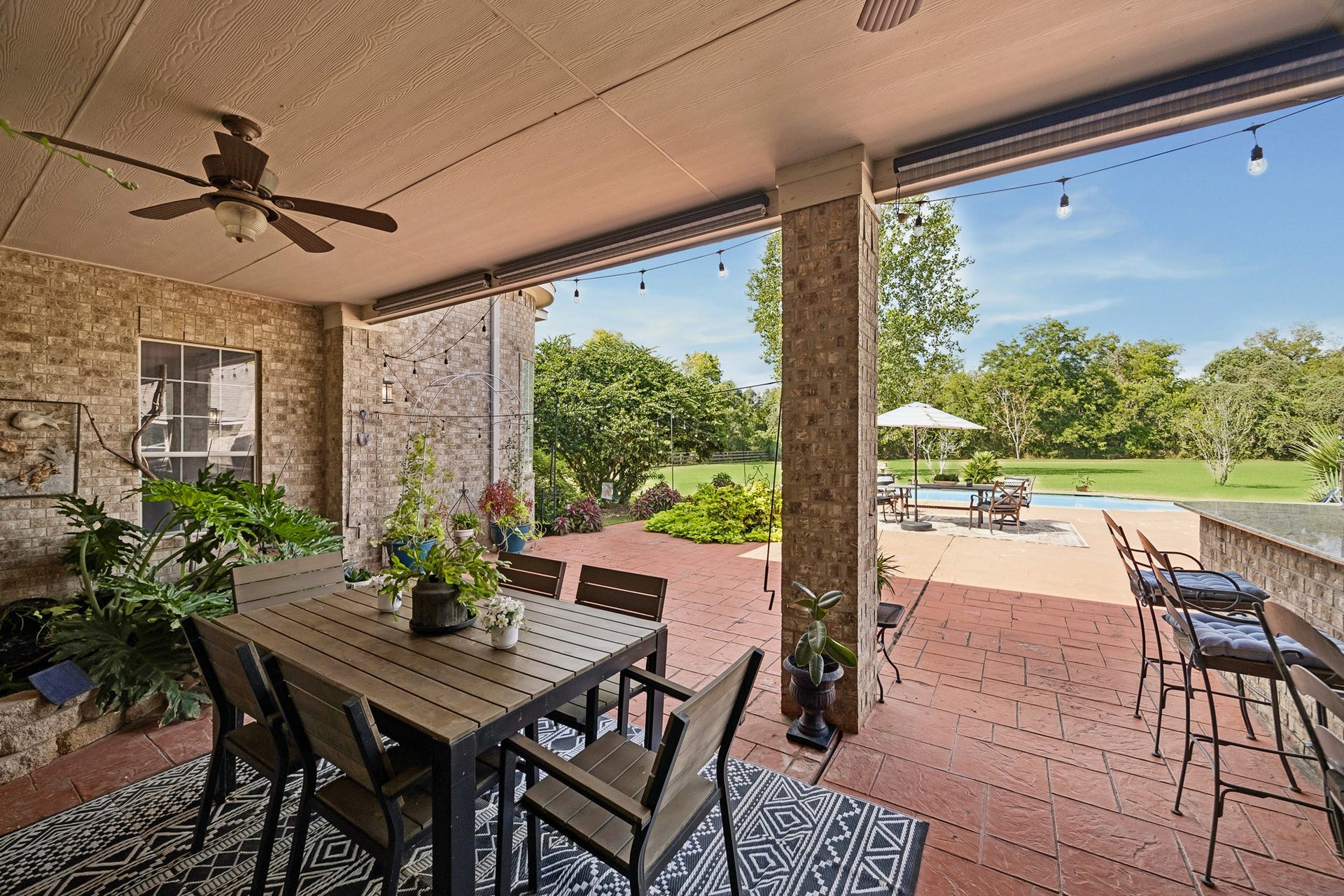 1319 Brazoswood Place, Richmond, TX 77406 An expansive covered patio offers an inviting space for outdoor entertaining, complete with multiple ceiling fans, dining and bar seating, and a brick fireplace. Three manual shades provide added privacy and shade, creating a comfortable outdoor retreat.