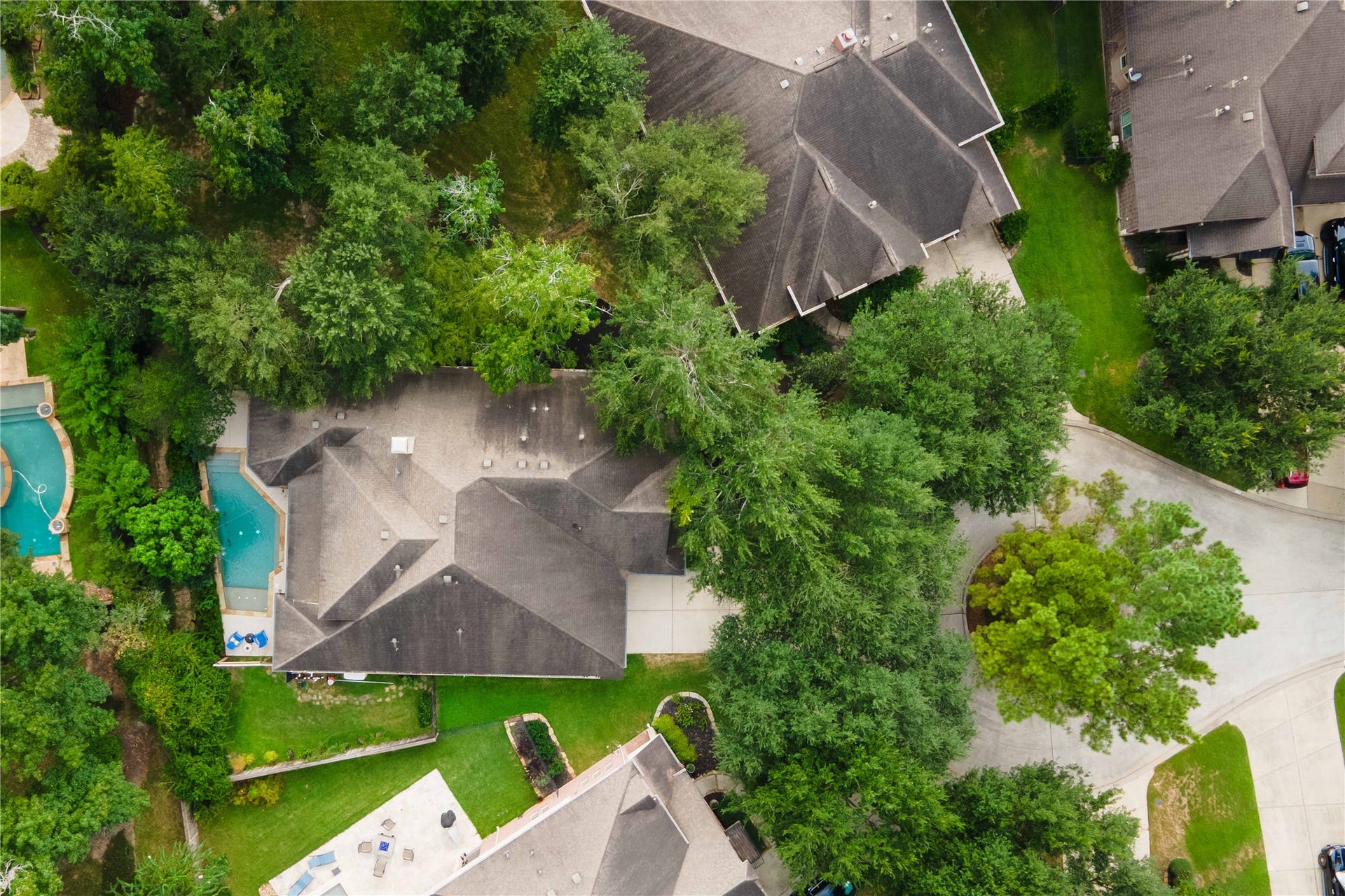 3 Blue Wildflower Pl, The Woodlands, TX 77354 This aerial view shows the home in the center surrounded by lawn space and mature trees, the private pool, and the cul-de-sac on the right.
