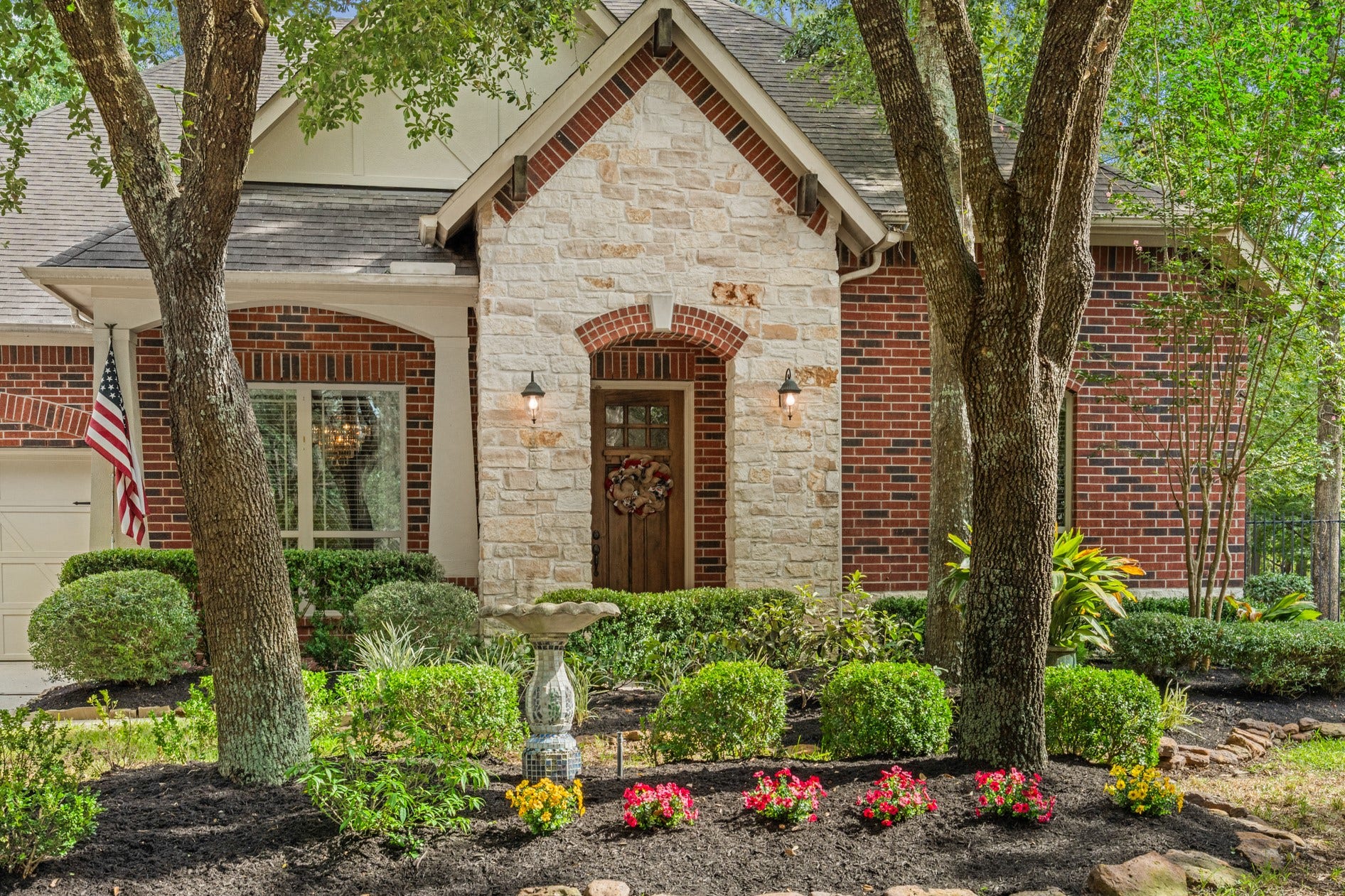3 Blue Wildflower Pl, The Woodlands, TX 77354 Curb appeal abounds with stone-lined flower beds and a stone and brick front elevation that also includes wood rafter accents and craftsman-style columns.
