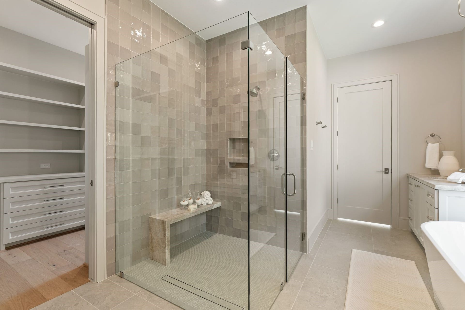 711 E 12th Street, Houston, TX 77008 Luxurious walk-in shower enclosed in glass, with layered stone-inspired tile, polished fixtures and a built-in bench.