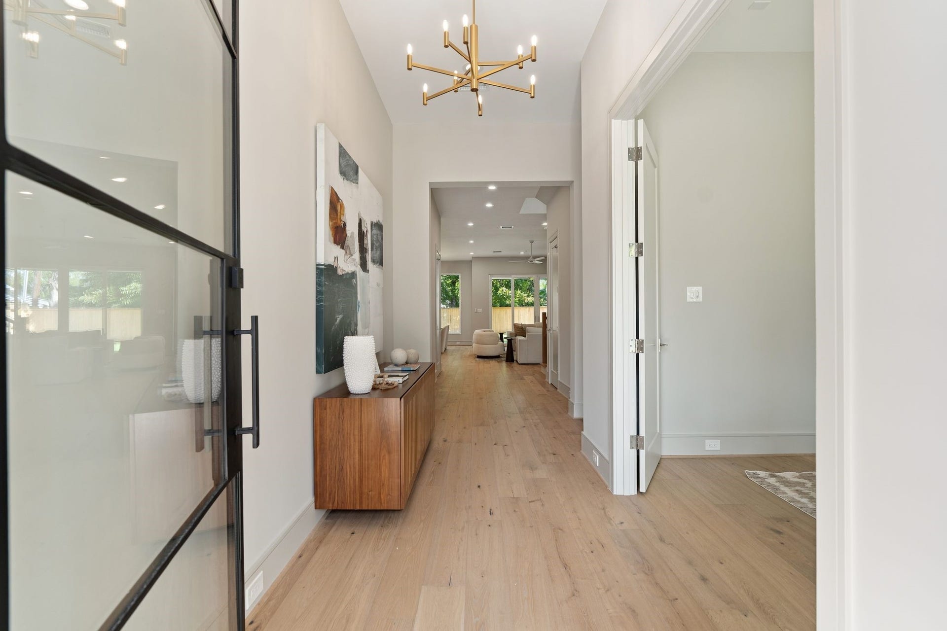 711 E 12th Street, Houston, TX 77008 An iron-and-glass front door opens to a bright, welcoming foyer crowned by a sculptural brass chandelier. Double doors lead into the home office, offering privacy just off the entry, while warm wood floors and an uninterrupted sightline toward the backyard draw you farther into the home.