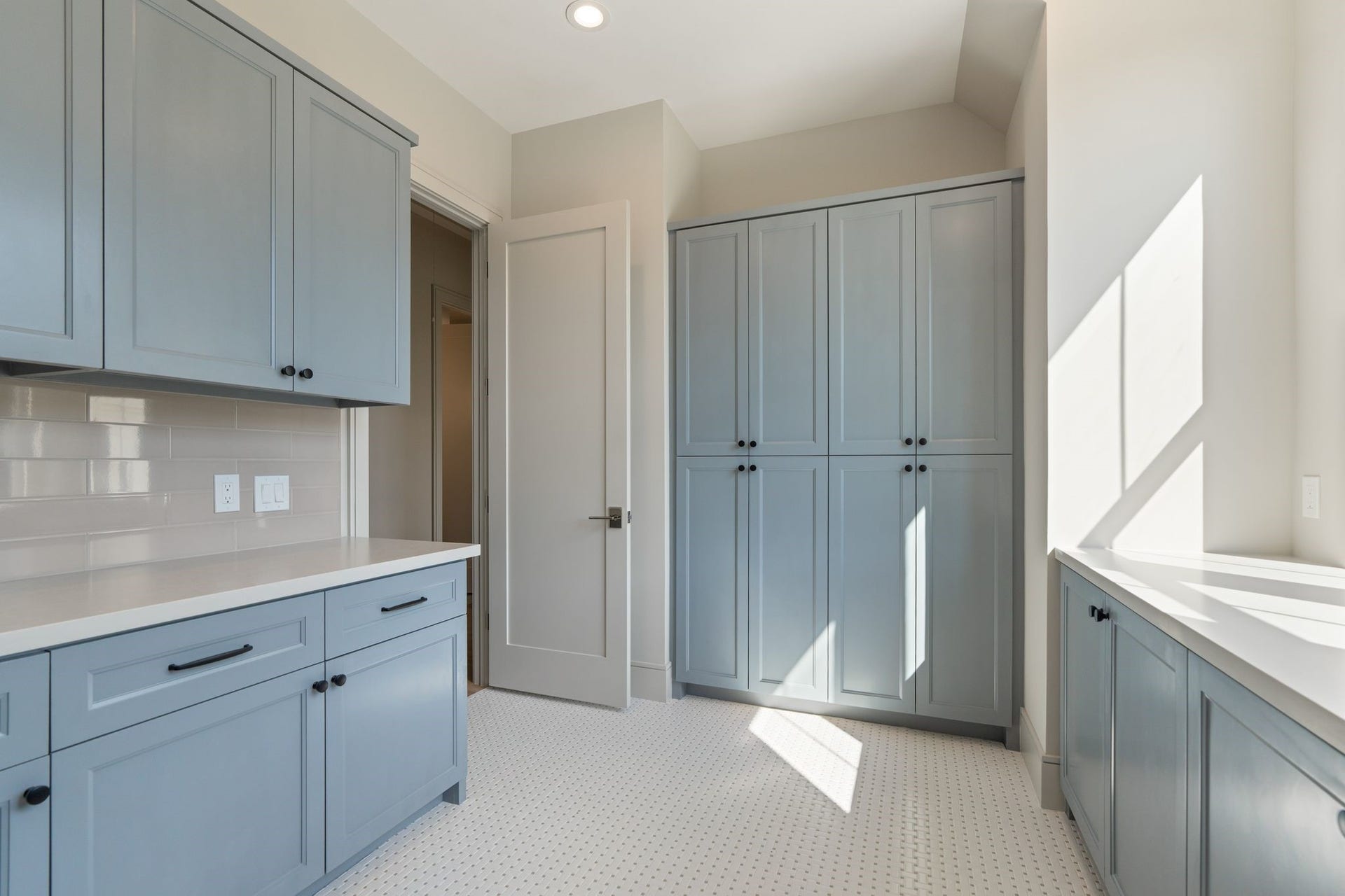 711 E 12th Street, Houston, TX 77008 A laundry room with room to spare: soft blue custom cabinetry, expansive quartz counters for folding, and tall cabinets to keep linens and supplies tucked away. Natural light and mosaic tile flooring make this hardworking space as inviting as it is practical.