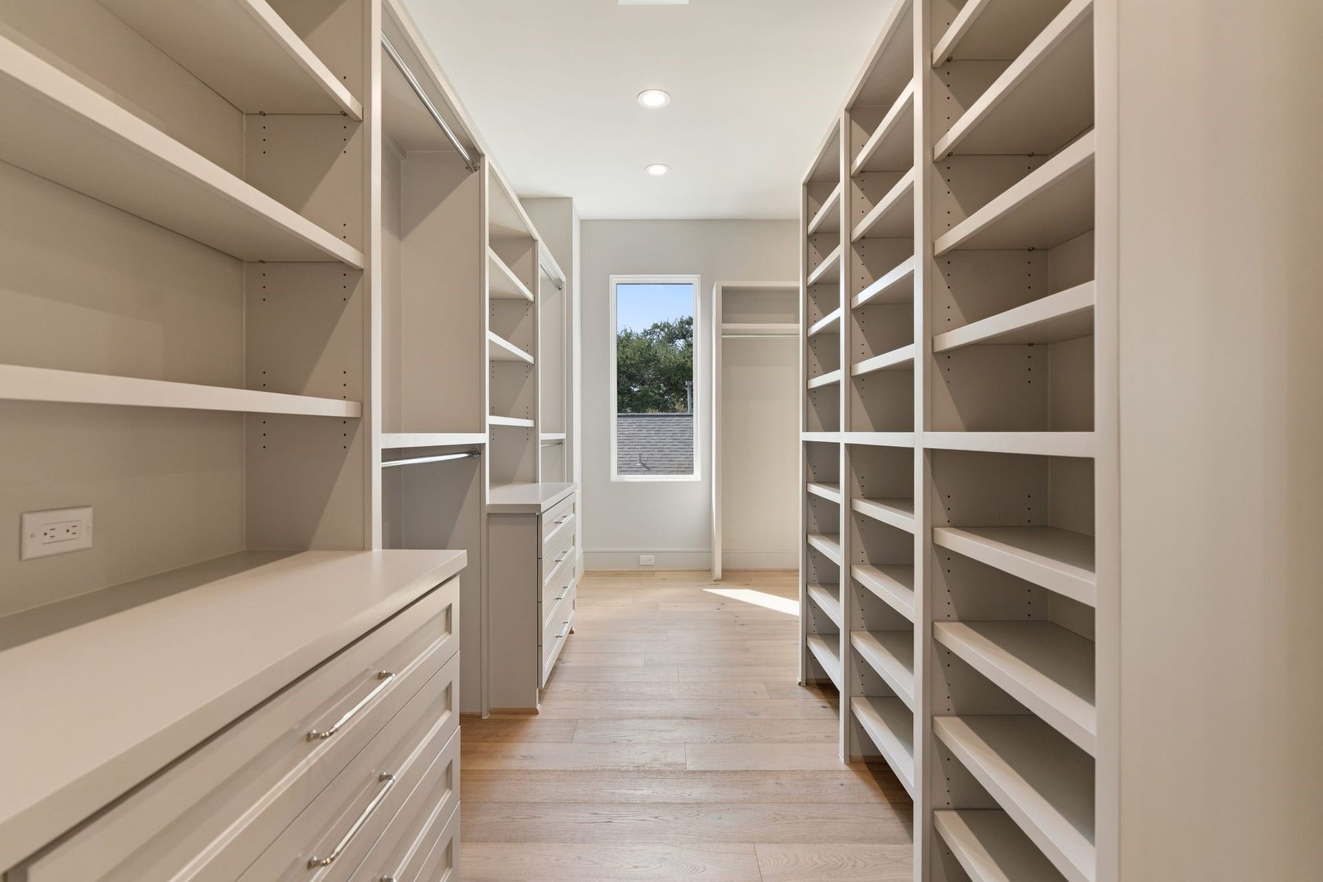 711 E 12th Street, Houston, TX 77008 An expansive walk-in closet brings boutique-style organization home, with floor-to-ceiling shelving, generous hanging space, and built-in drawers. Warm hardwood floors and a window at the far end make this everyday luxury feel bright and inviting.