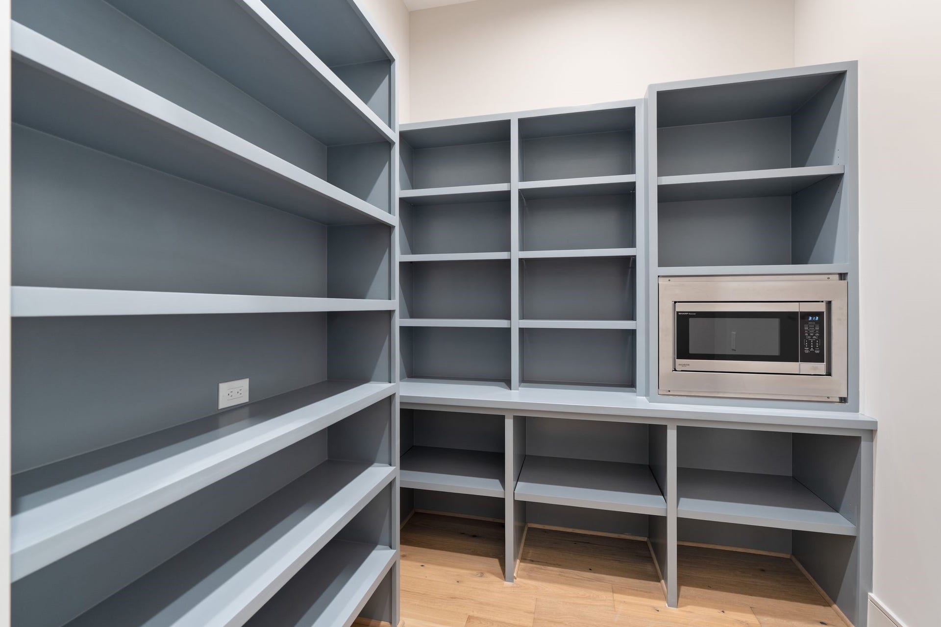 711 E 12th Street, Houston, TX 77008 This spacious walk-in pantry features extensive shelving in Sherwin-Williams Cadet, a built-in microwave, and outlets for countertop appliances keeping kitchen counters clear and everyday essentials within easy reach.